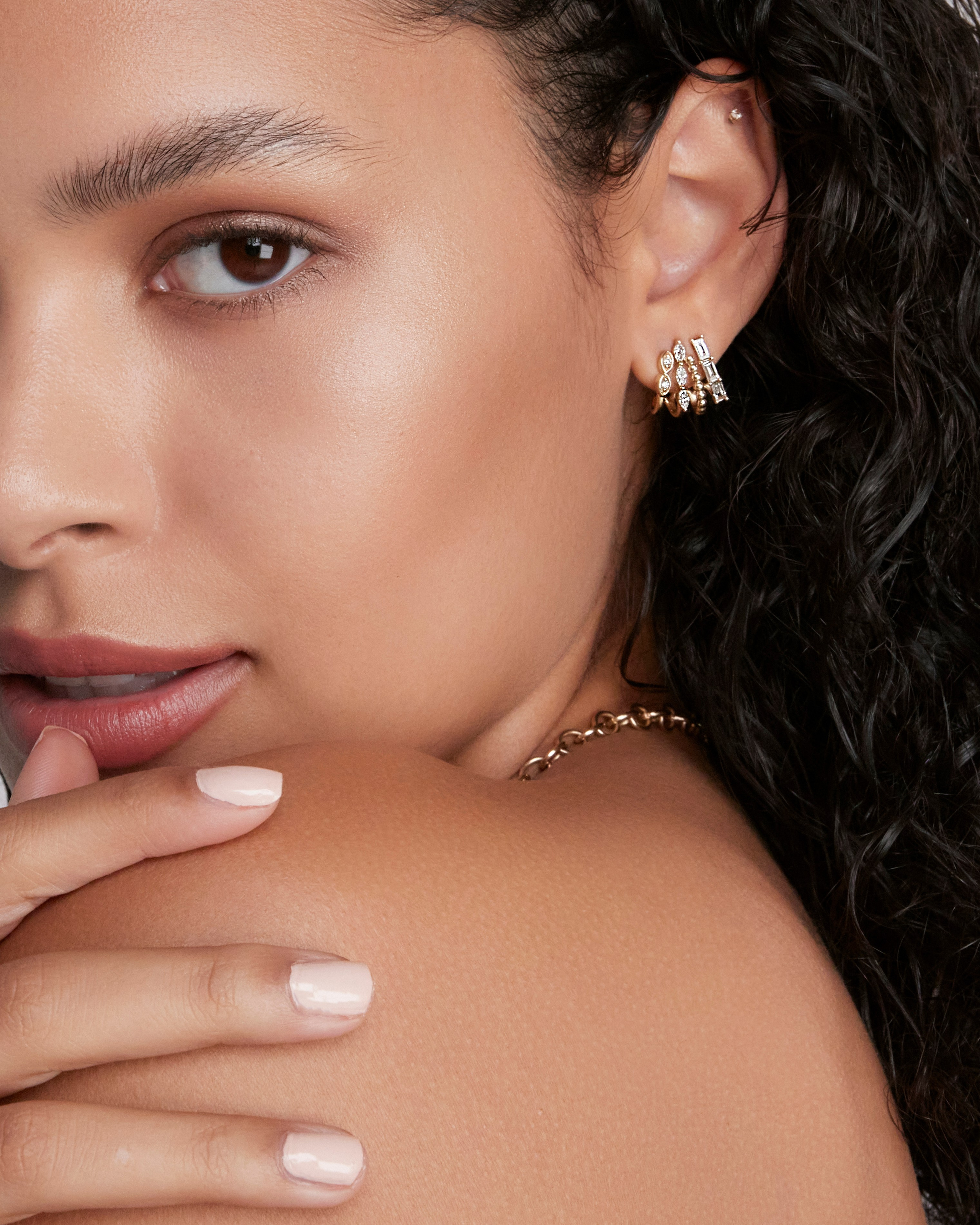 Close-up of a model highlighting a gold earring with flawless makeup, emphasizing understated elegance.