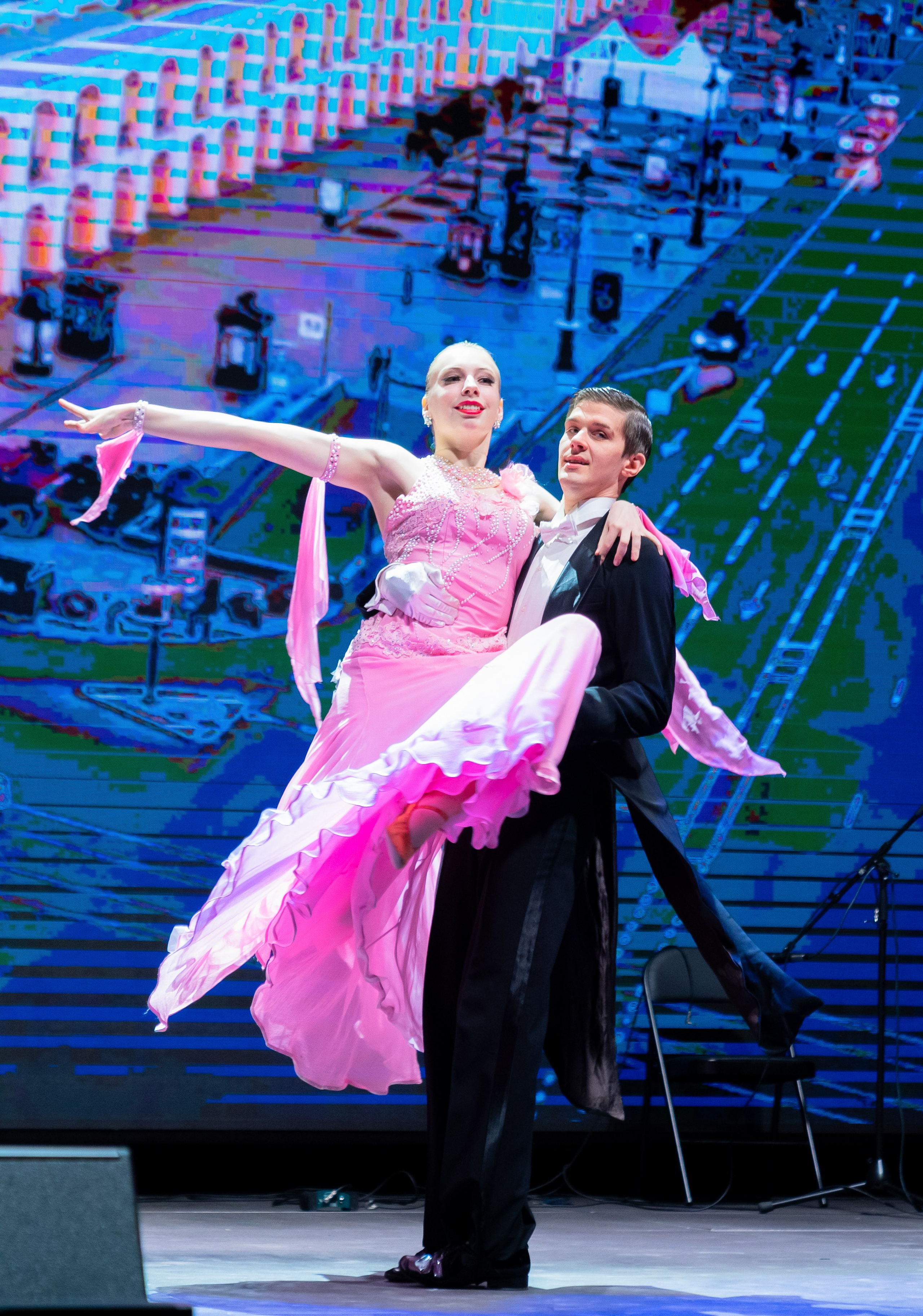 Бальный танец: партнёр держит партнёршу на руках. Яркий розовый наряд с лентами, большой LED-экран на заднем плане. День местного самоуправления в Санкт-Петербурге. Фото Евгения Мальцева.