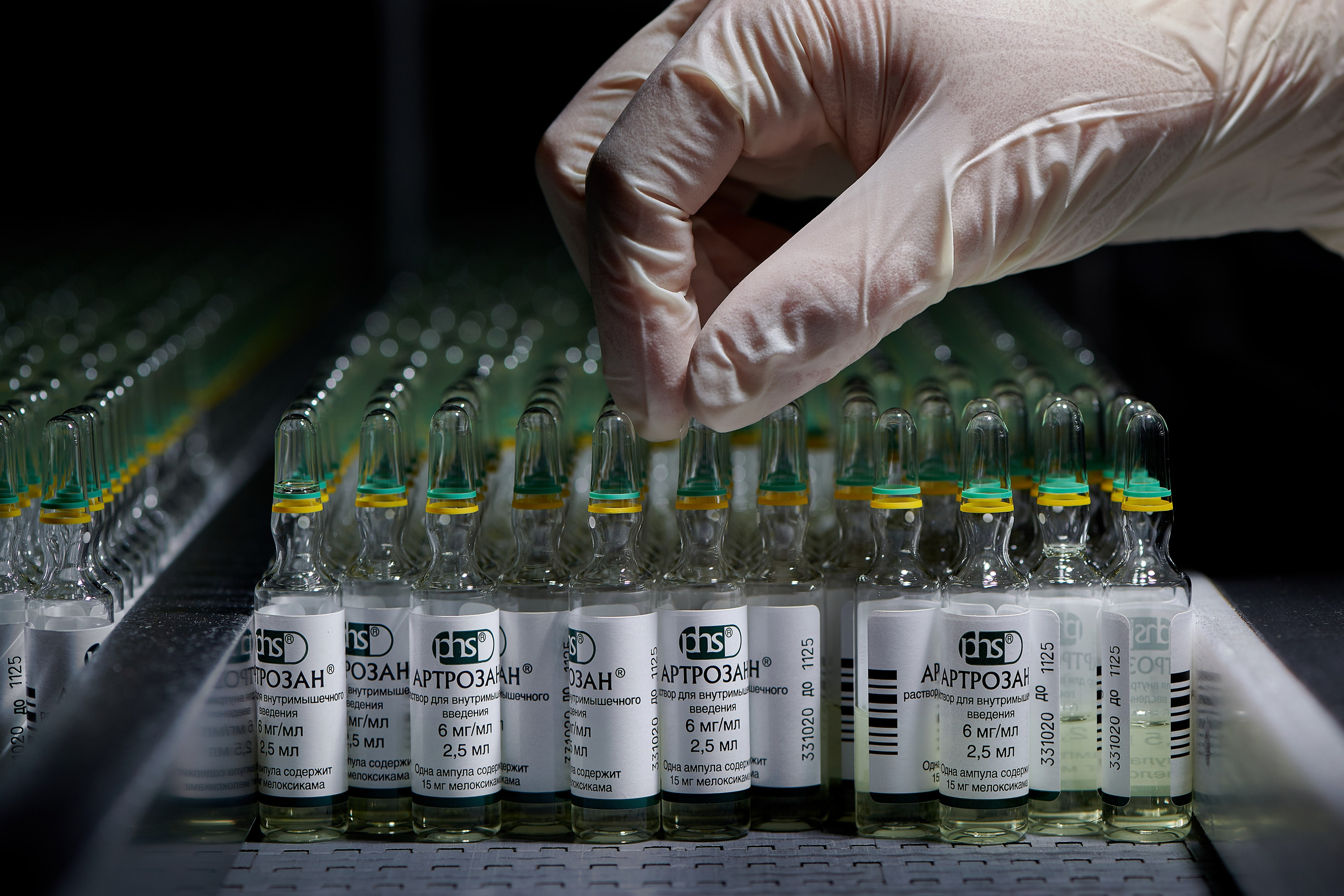рука сотрудника фармоцевтической компании в перчатке поворачивает ампулы с лекарством