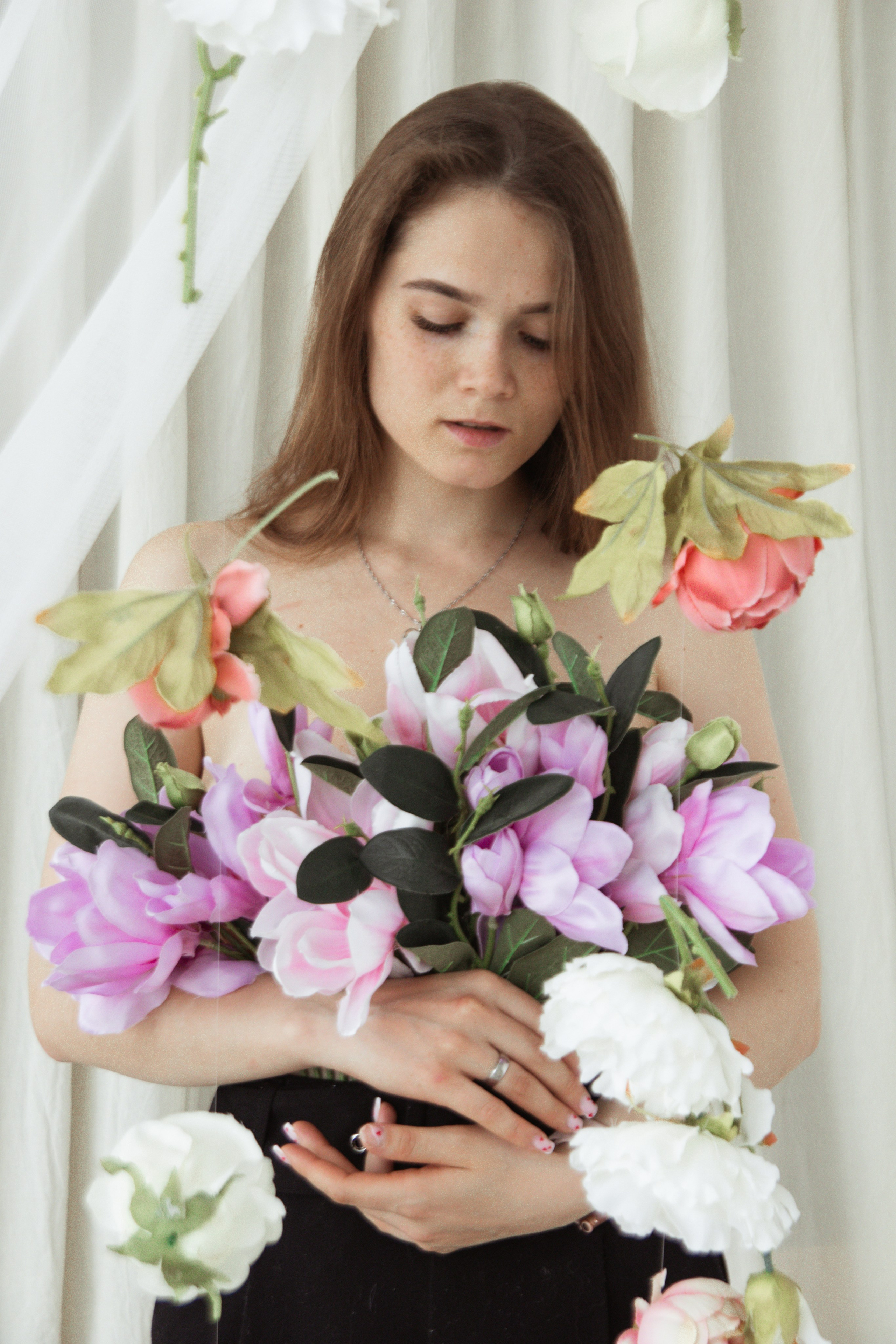 девушка фотографируется на белом фоне с цветами и лианами из цветов в фотостудии