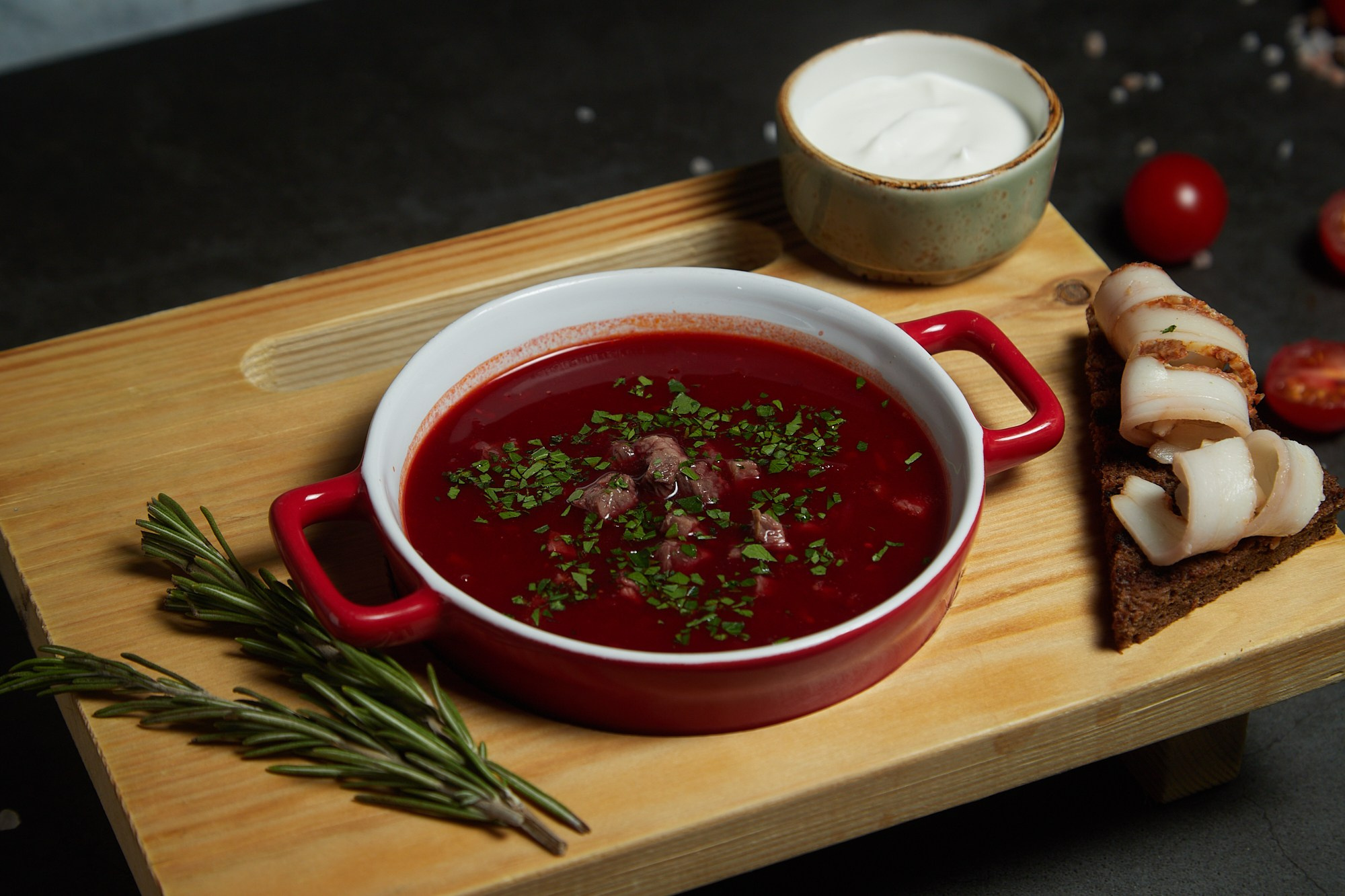 Фуд-фотография борща со сметаной и зеленью в глубокой миске.