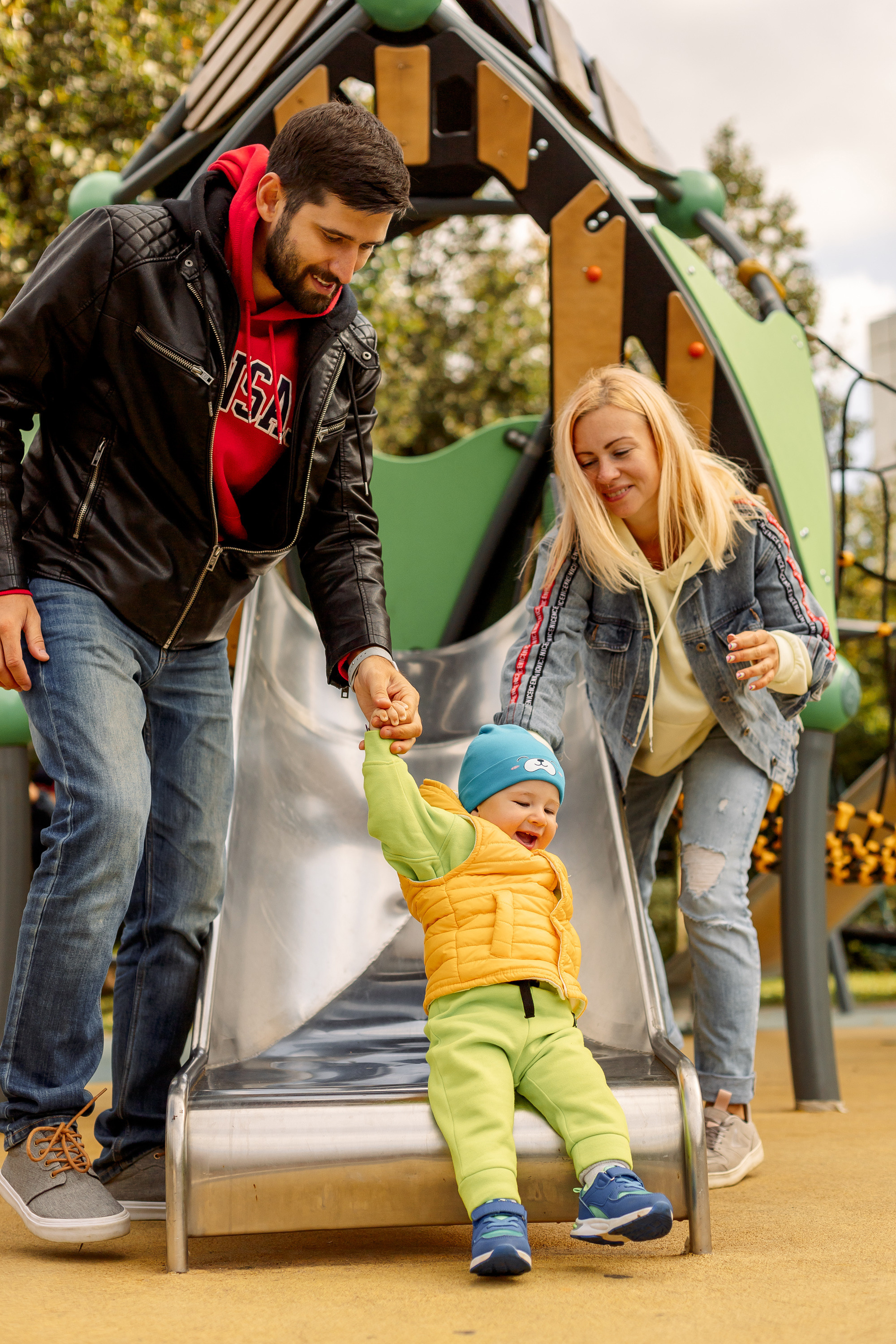 сын за руки  съезжает с горки 