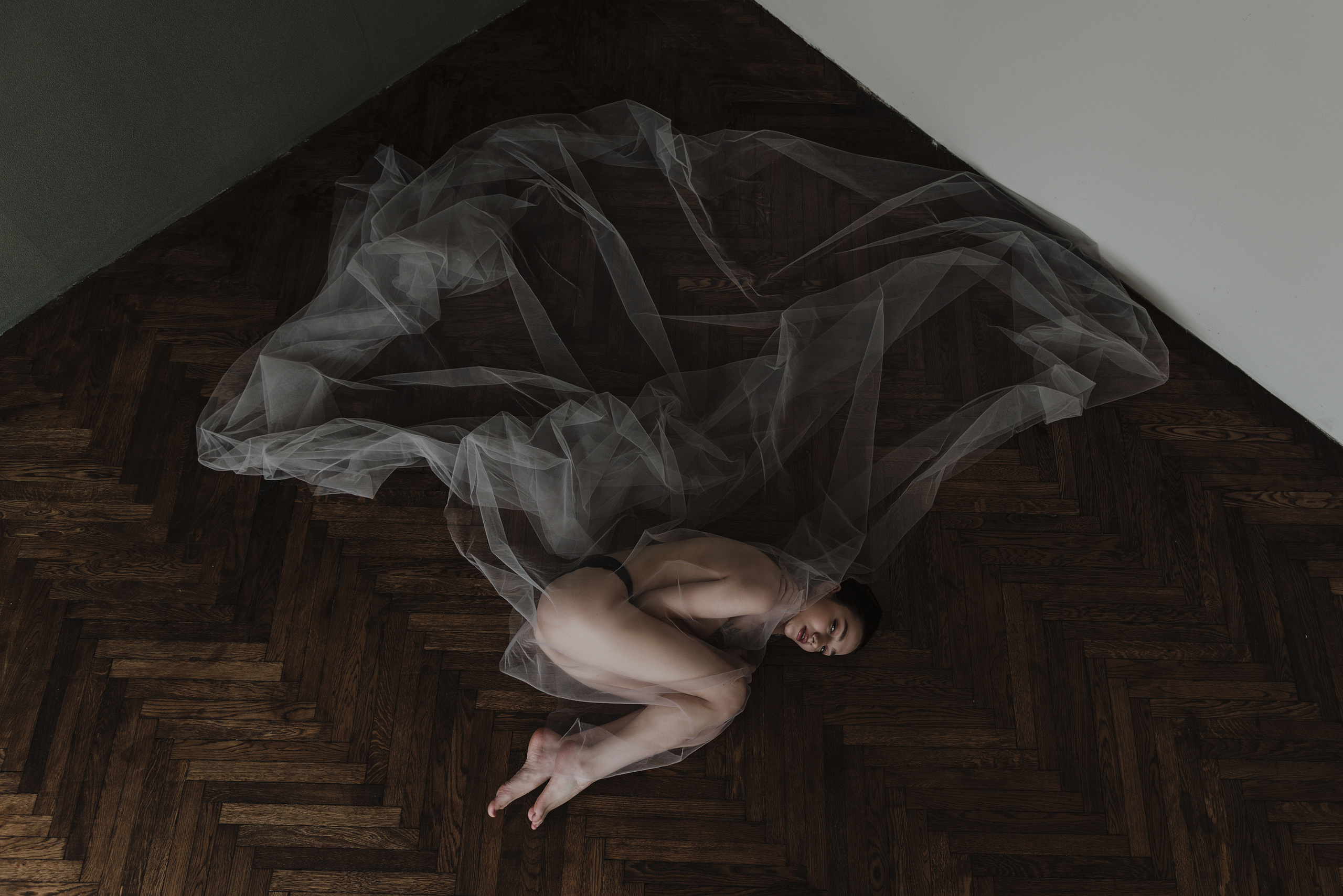 Красивая серая ткань развивается по полу, где лежит полуголая девушка.