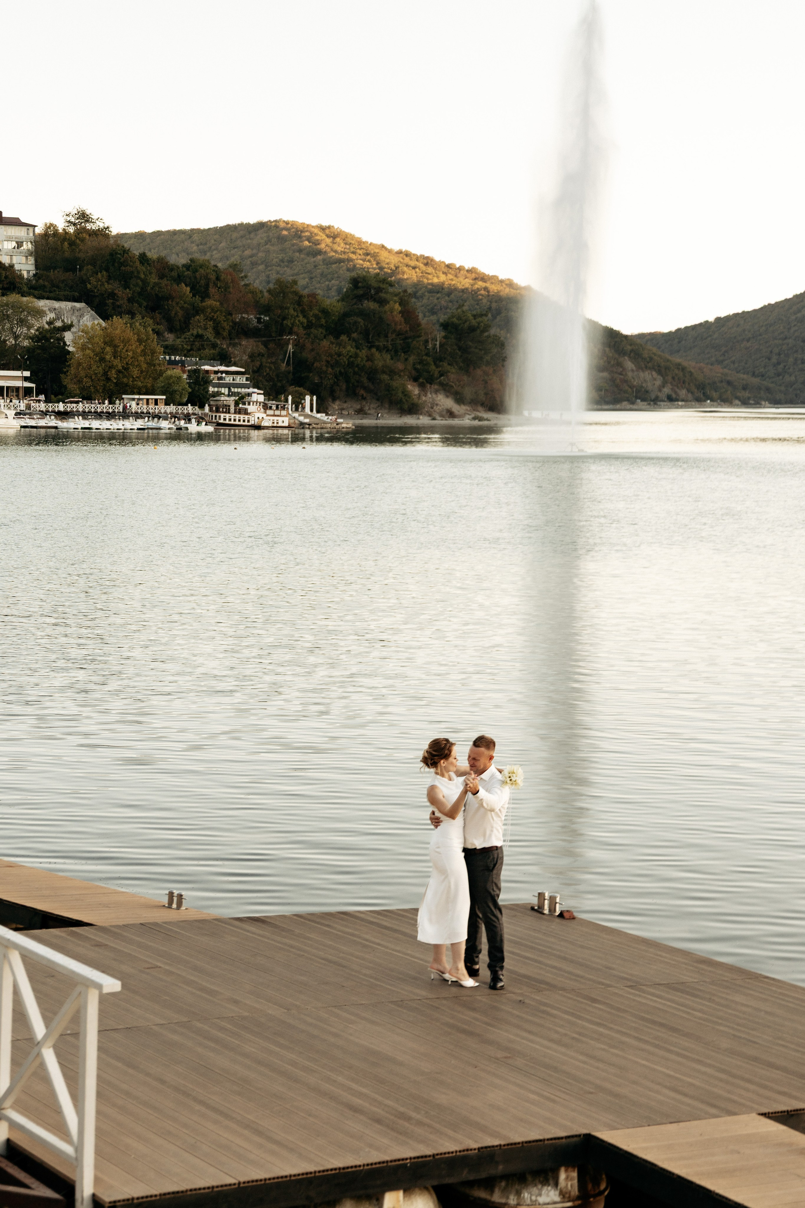 Жених нежно обнимает невесту на фоне гор и озера