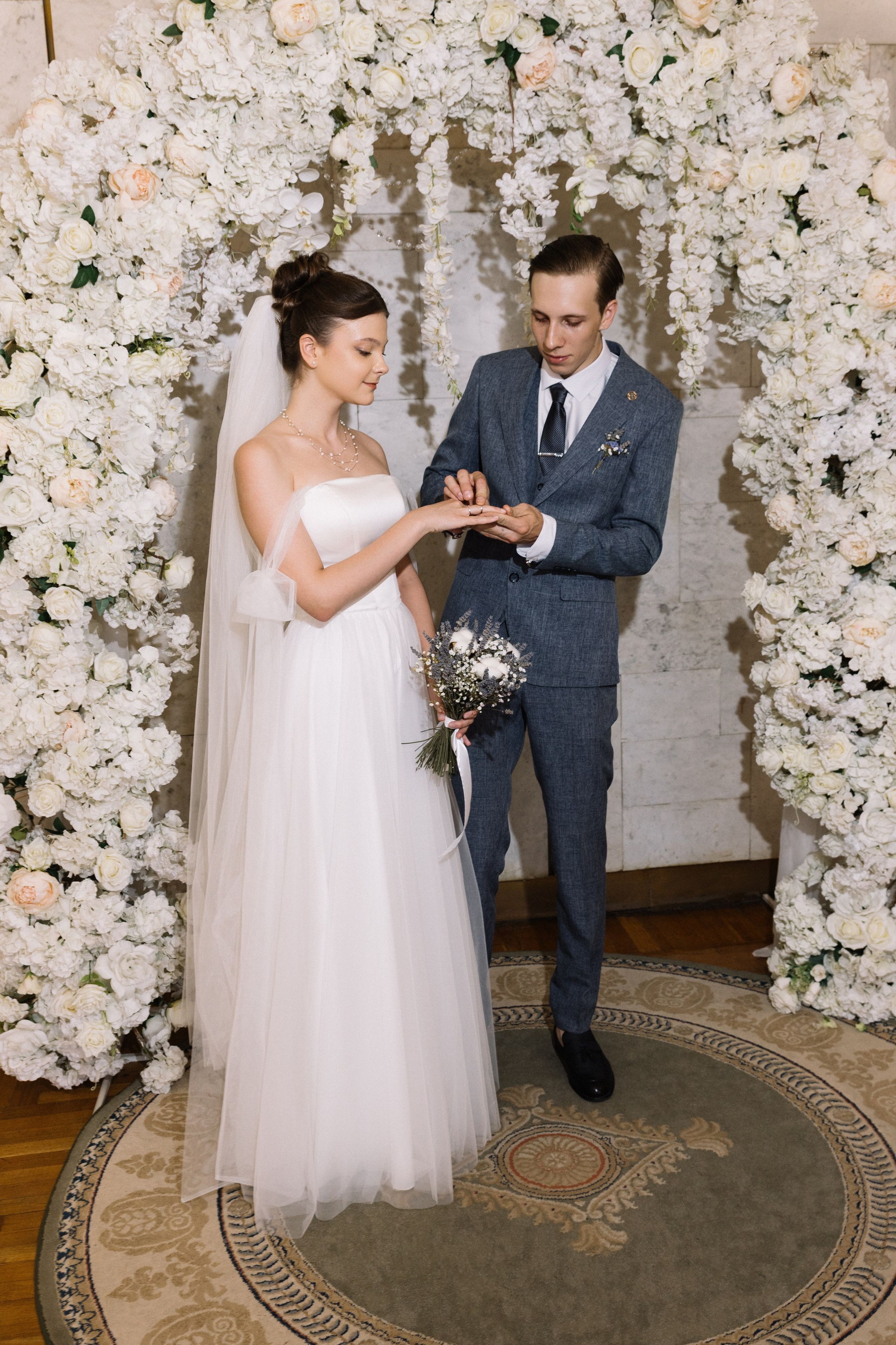 На фоне цветочной арки Мартин надевает обручальное кольцо своей супруге