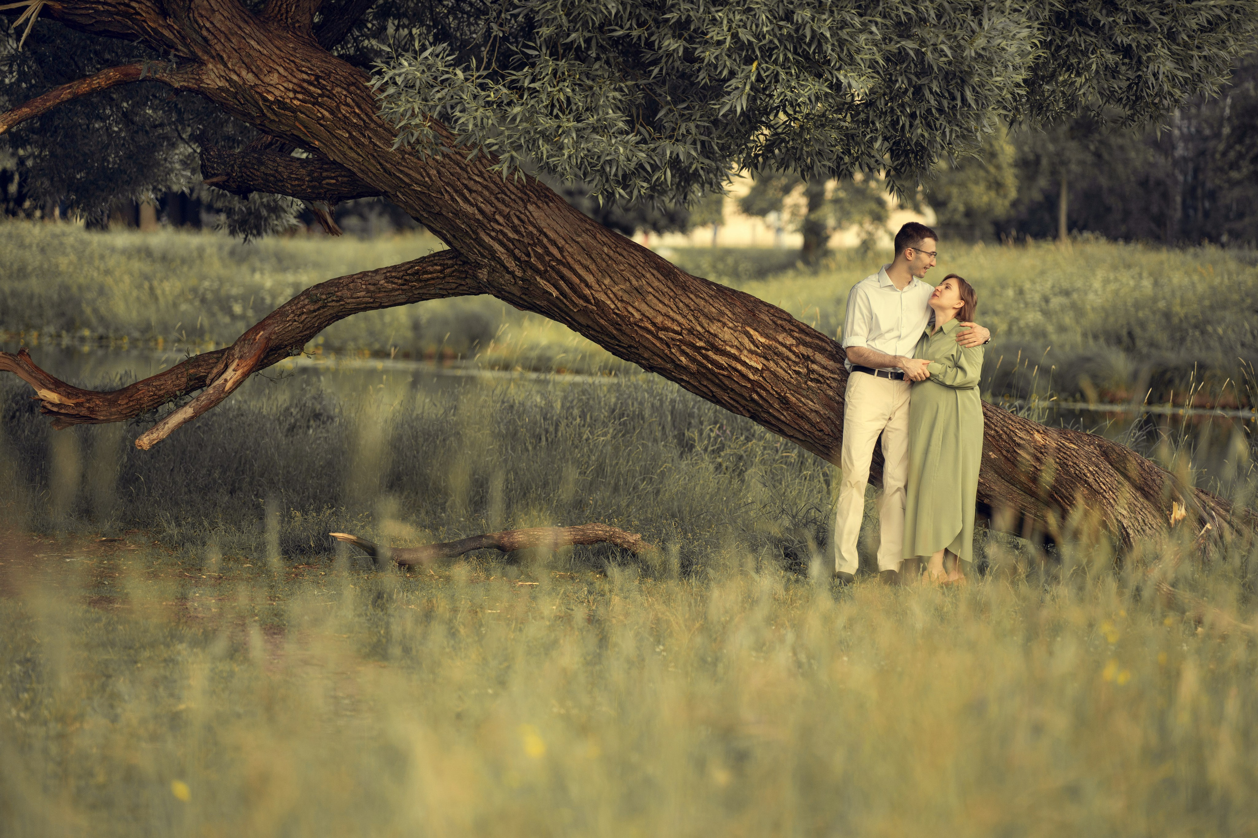 Семейная пара на прогулке с парке. Женщина беременная обнимает мужа.