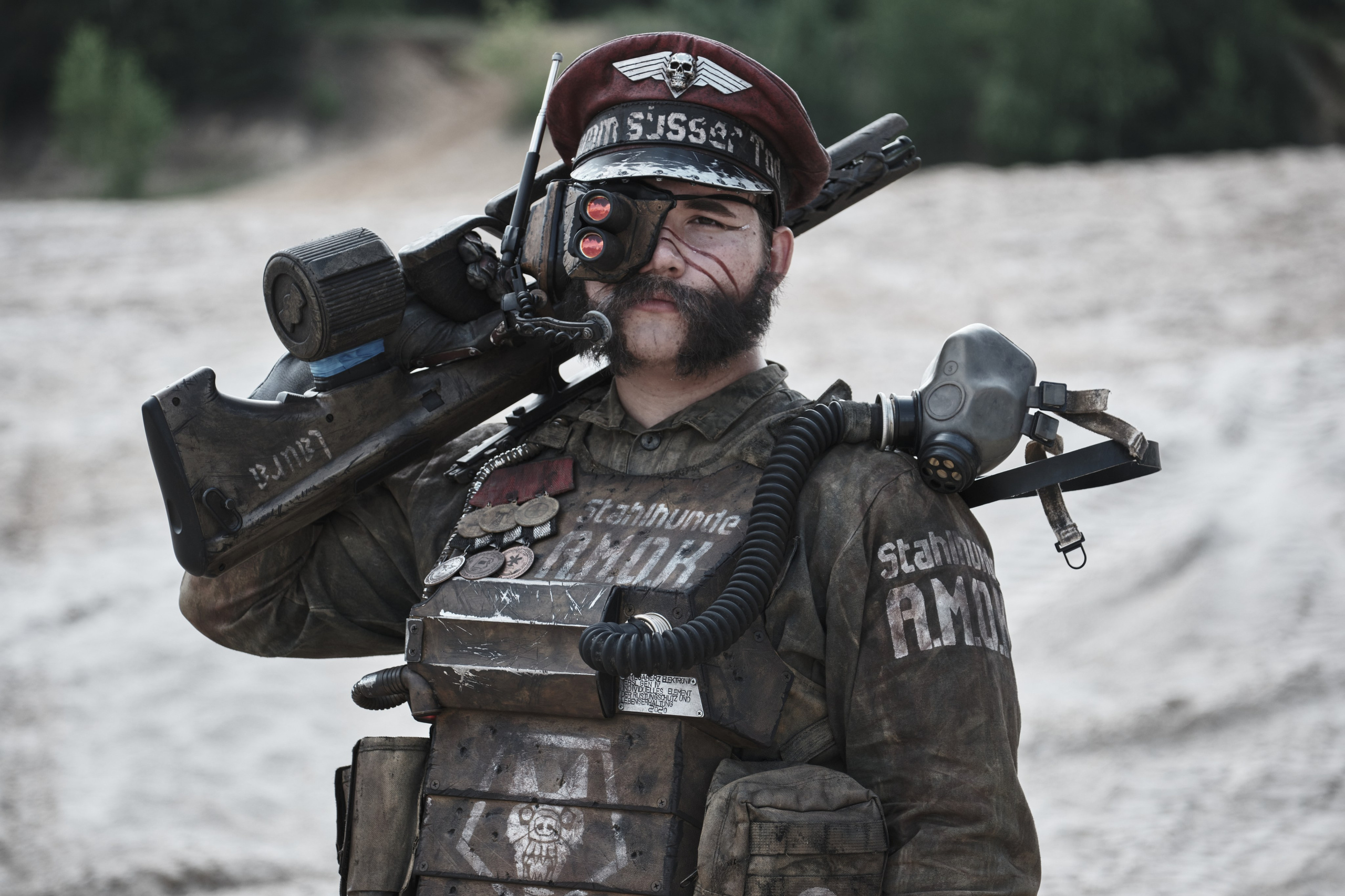 Мужчина в боевом костюме с автоматом на плече смотрит в камеру