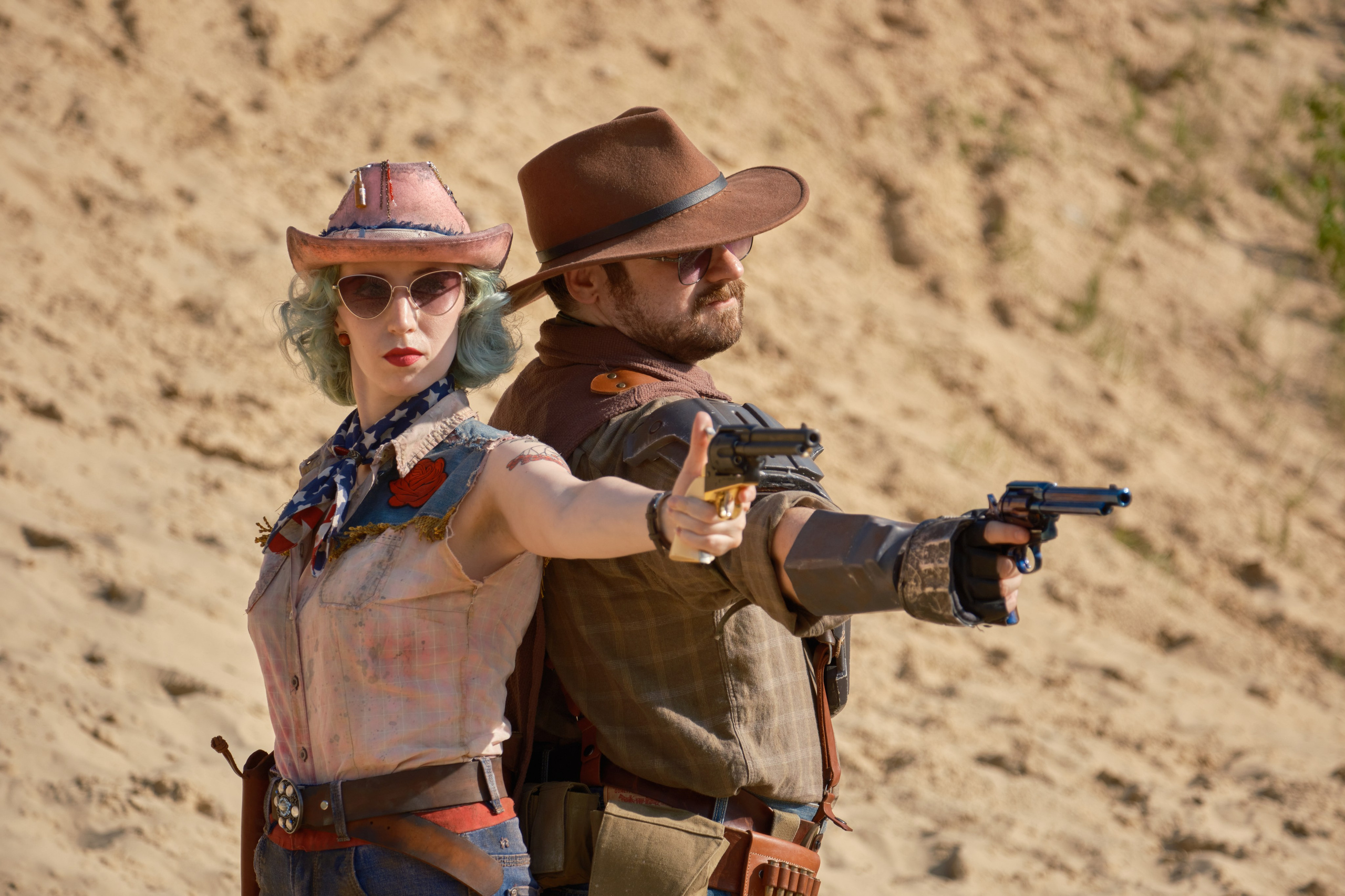 Мужчина и девушка в ковбойских шляпах и револьверами стоят спина к спине и целятся из револьверов