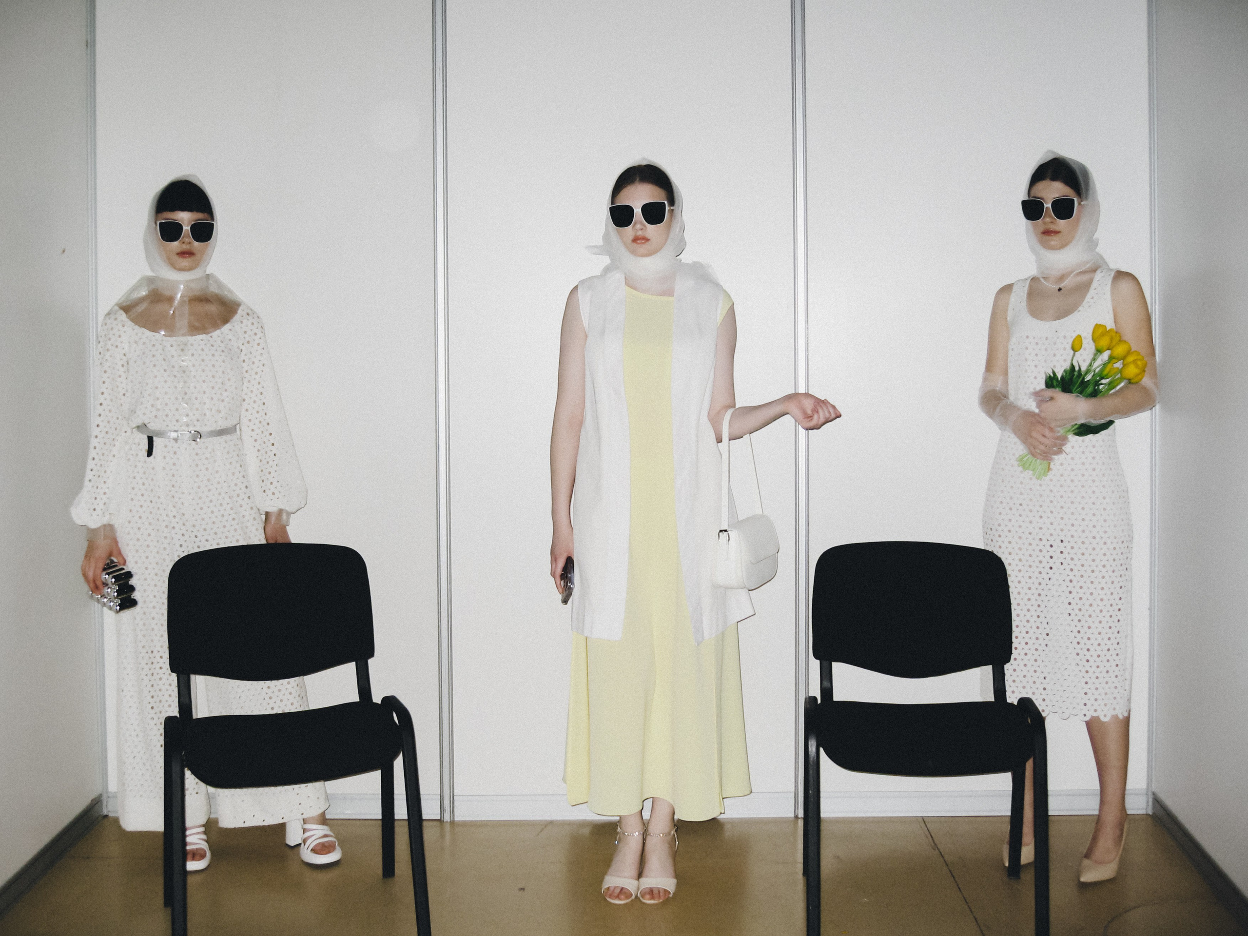 ростовой портрет три девушки в темных очках и косынках стоят на фоне белой стены между черными стульями