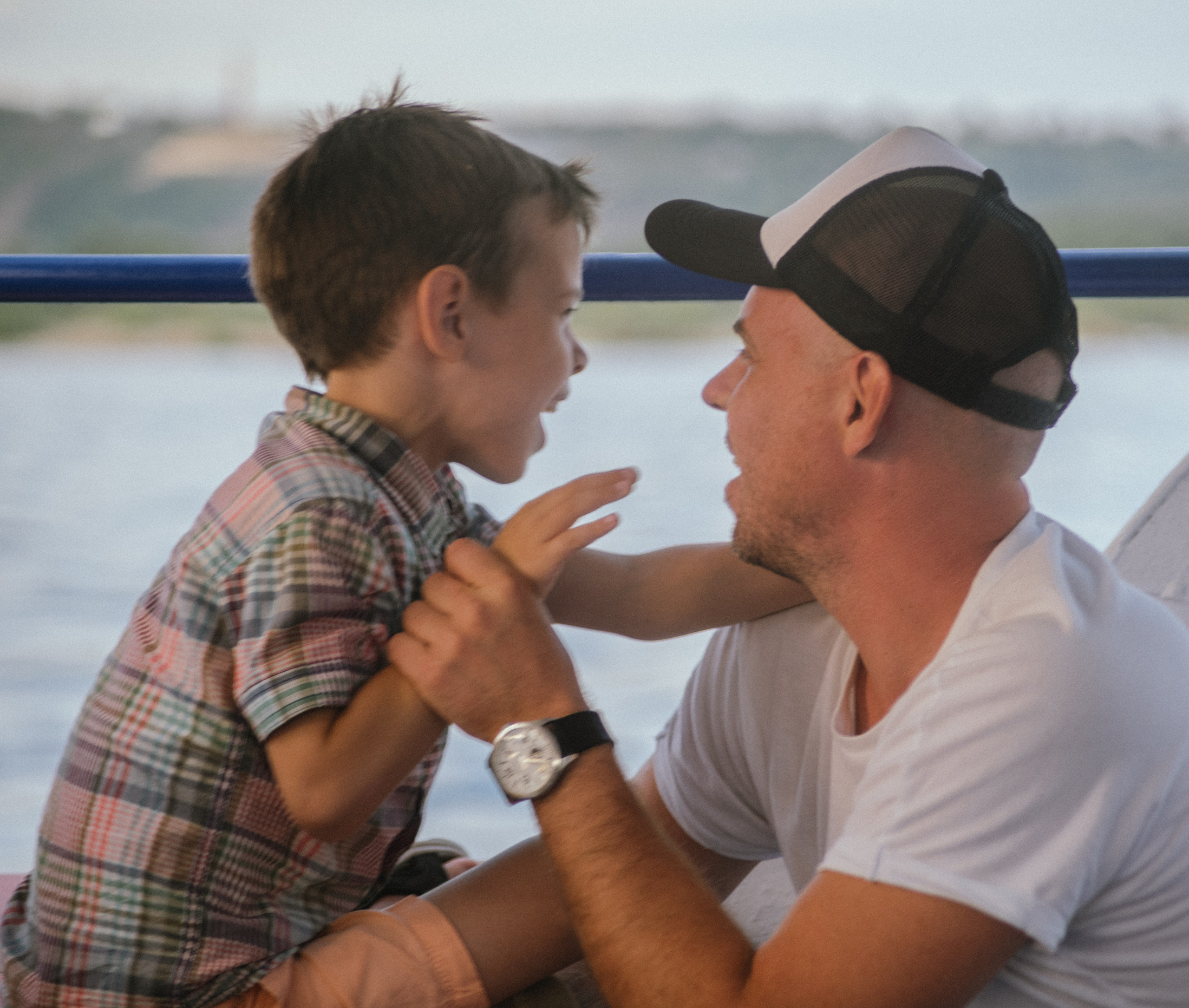 Отец и сын внимательно смотрят друг другу в глаза — тёплый и доверительный диалог на фоне реки.