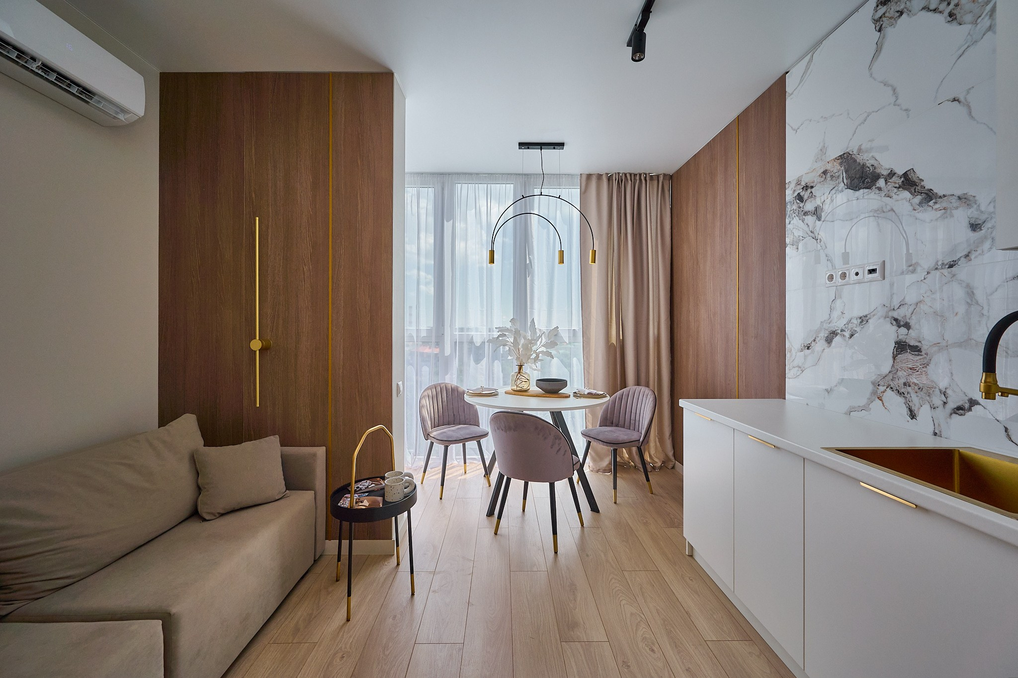 кухня светлые оттенки бежевый диван белые плиты белые полки и шкафы круглый белый стол с розовыми стульями светлые шторы