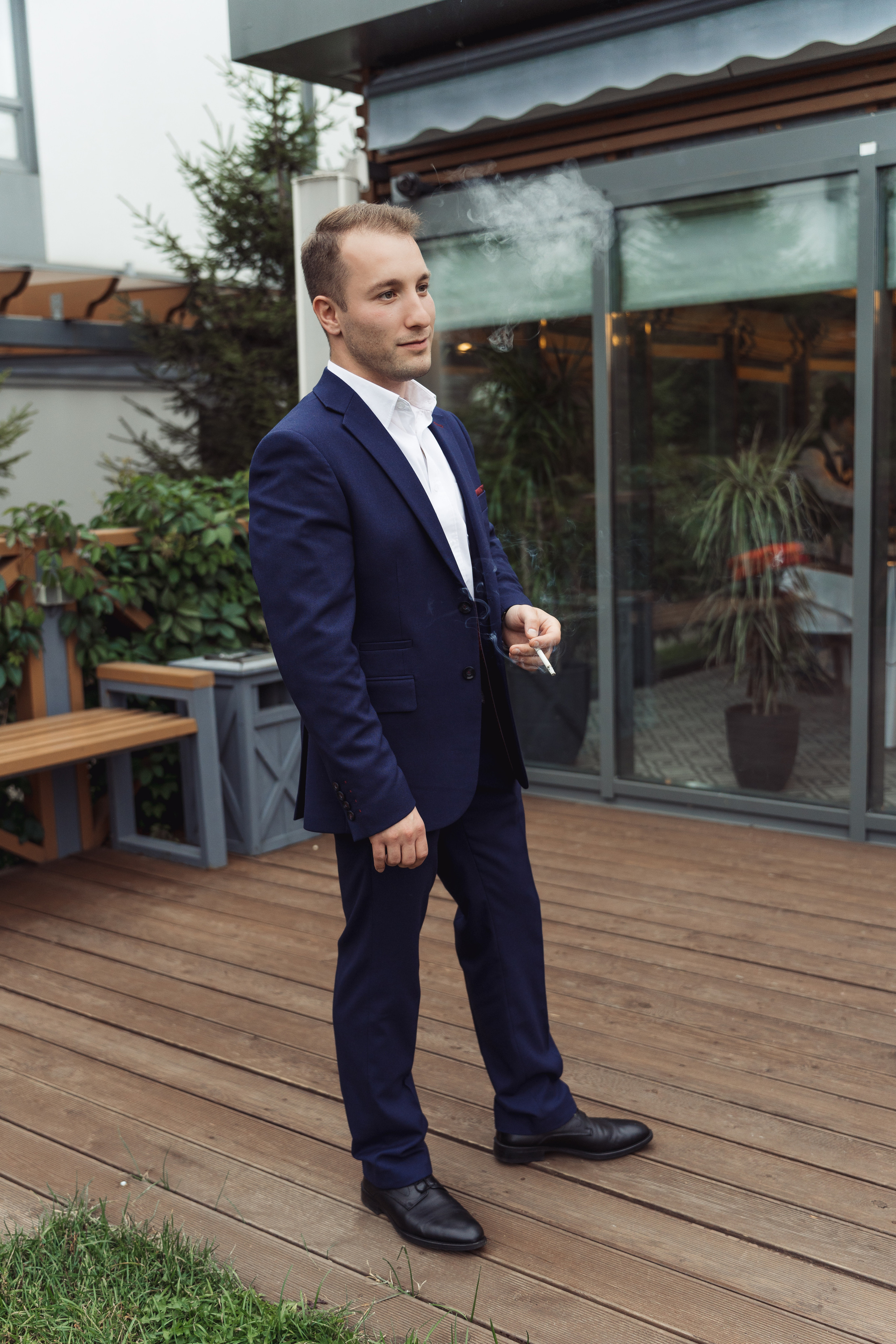 Друг жениха курит и смотрит на свадебный банкет