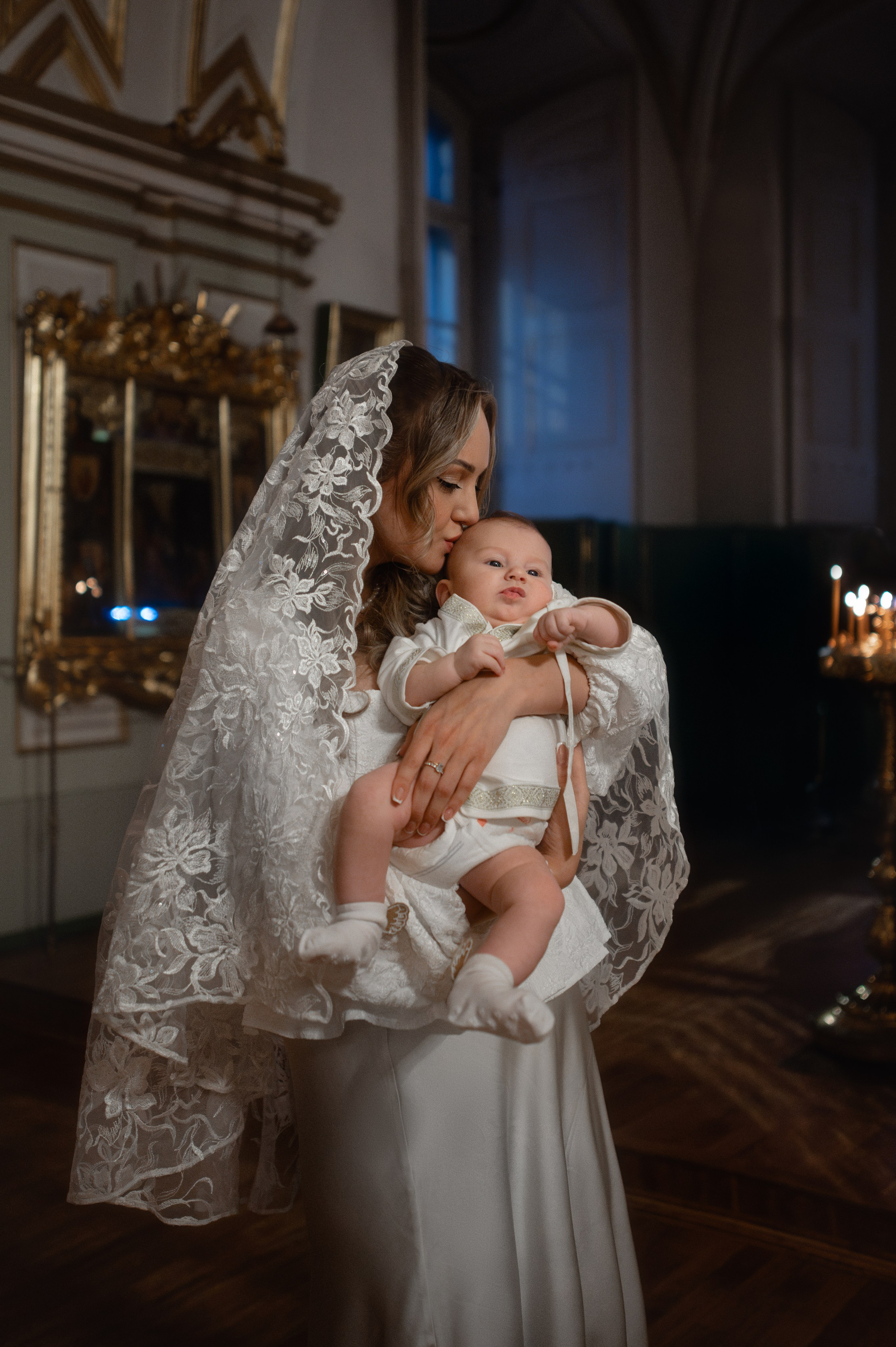 Мама целует малыша в храме на фоне свечей