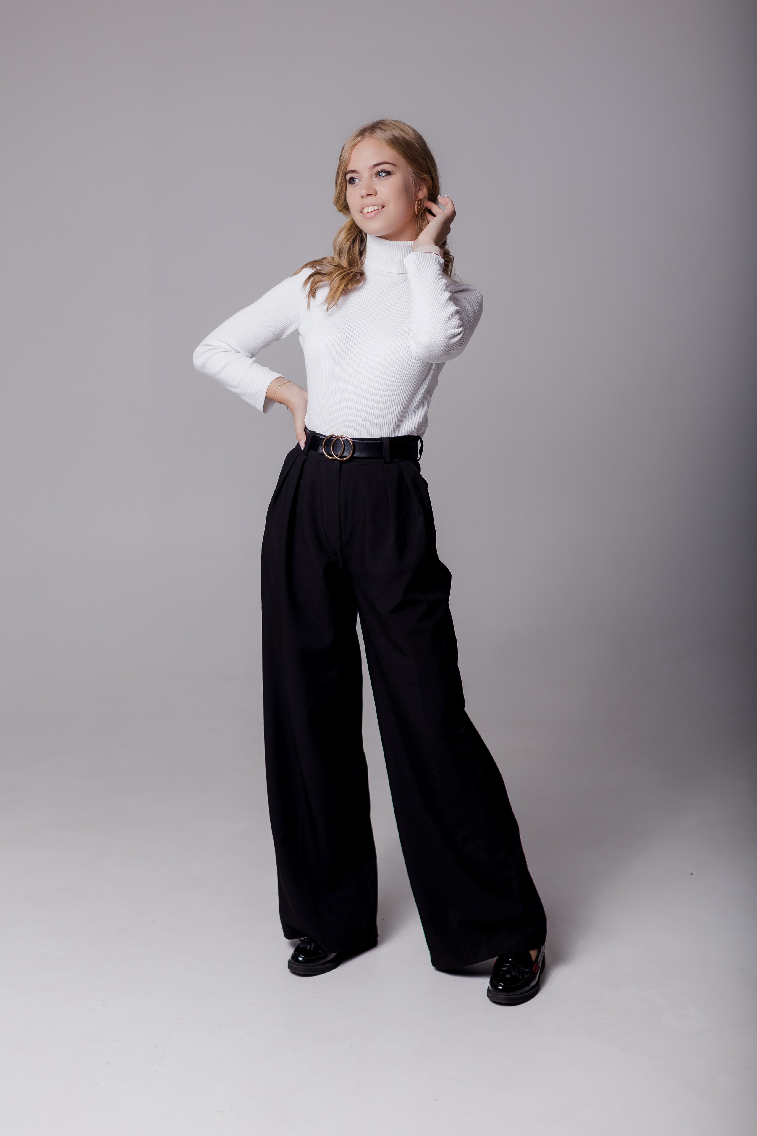 Девушка стоит в полный рост в фотостудии с нейтральным фоном