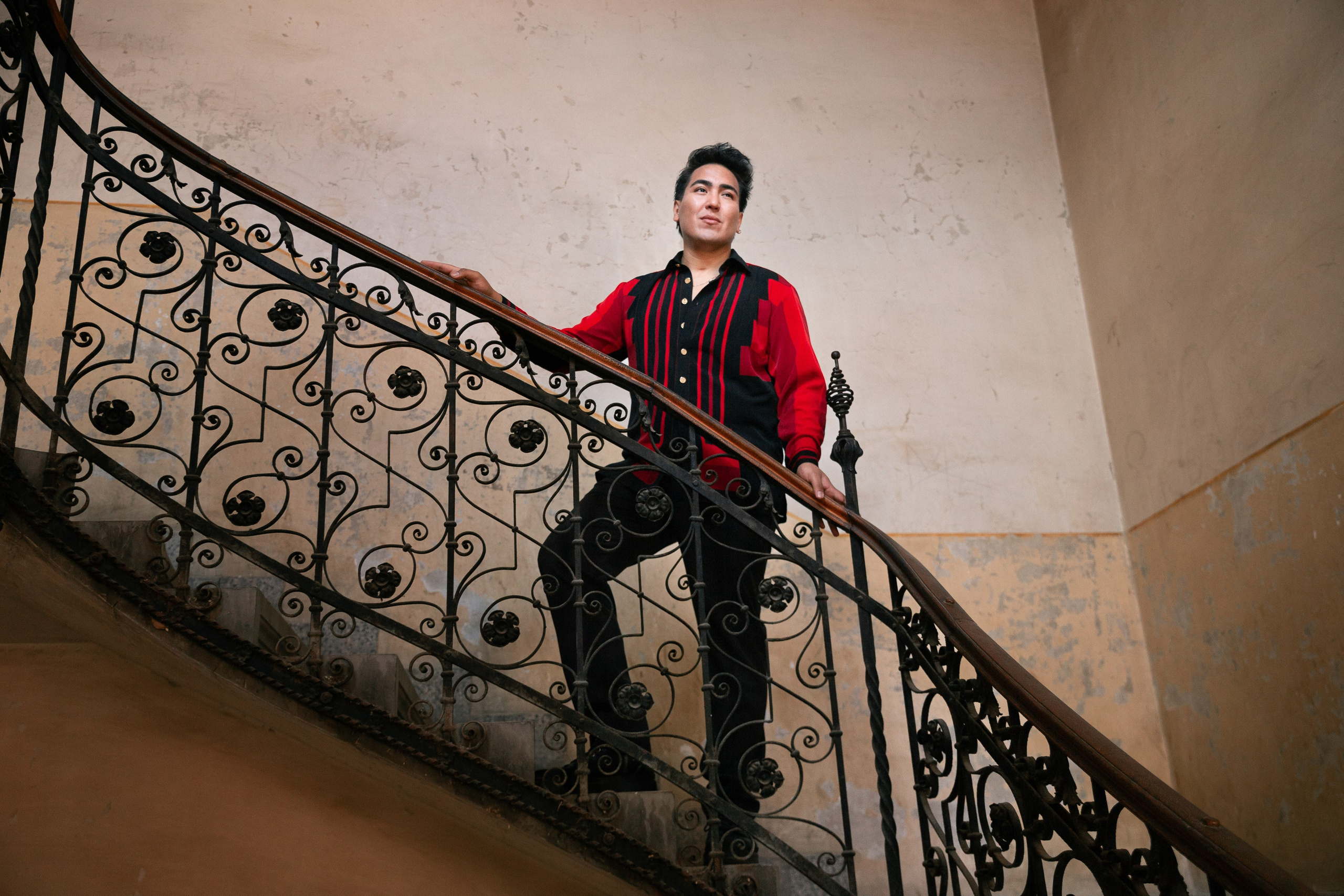 a portrait of a man in a red shirt standing on a spiral staircase
