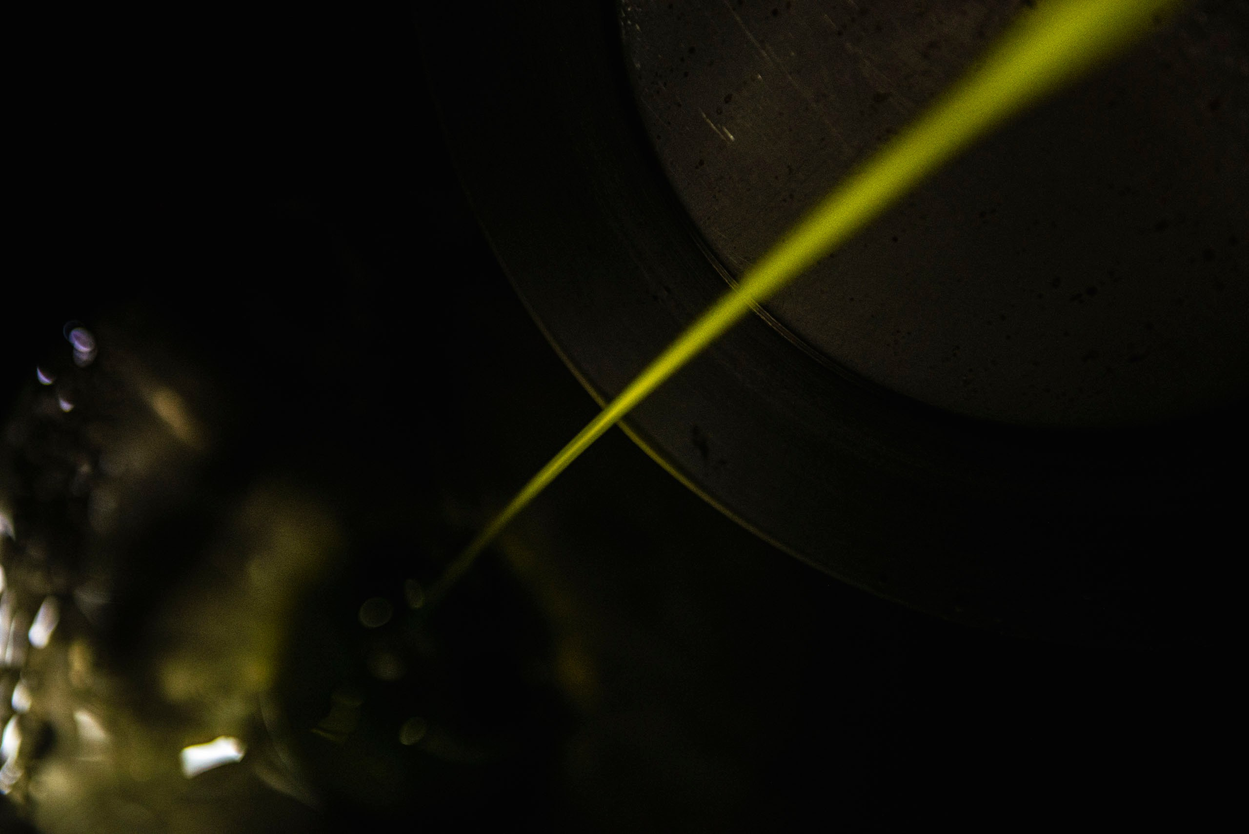 Крупный план ярко-салатовой струи свежевыжатого оливкового масла первого холодного отжима, вытекающей из оборудования на темном фоне.