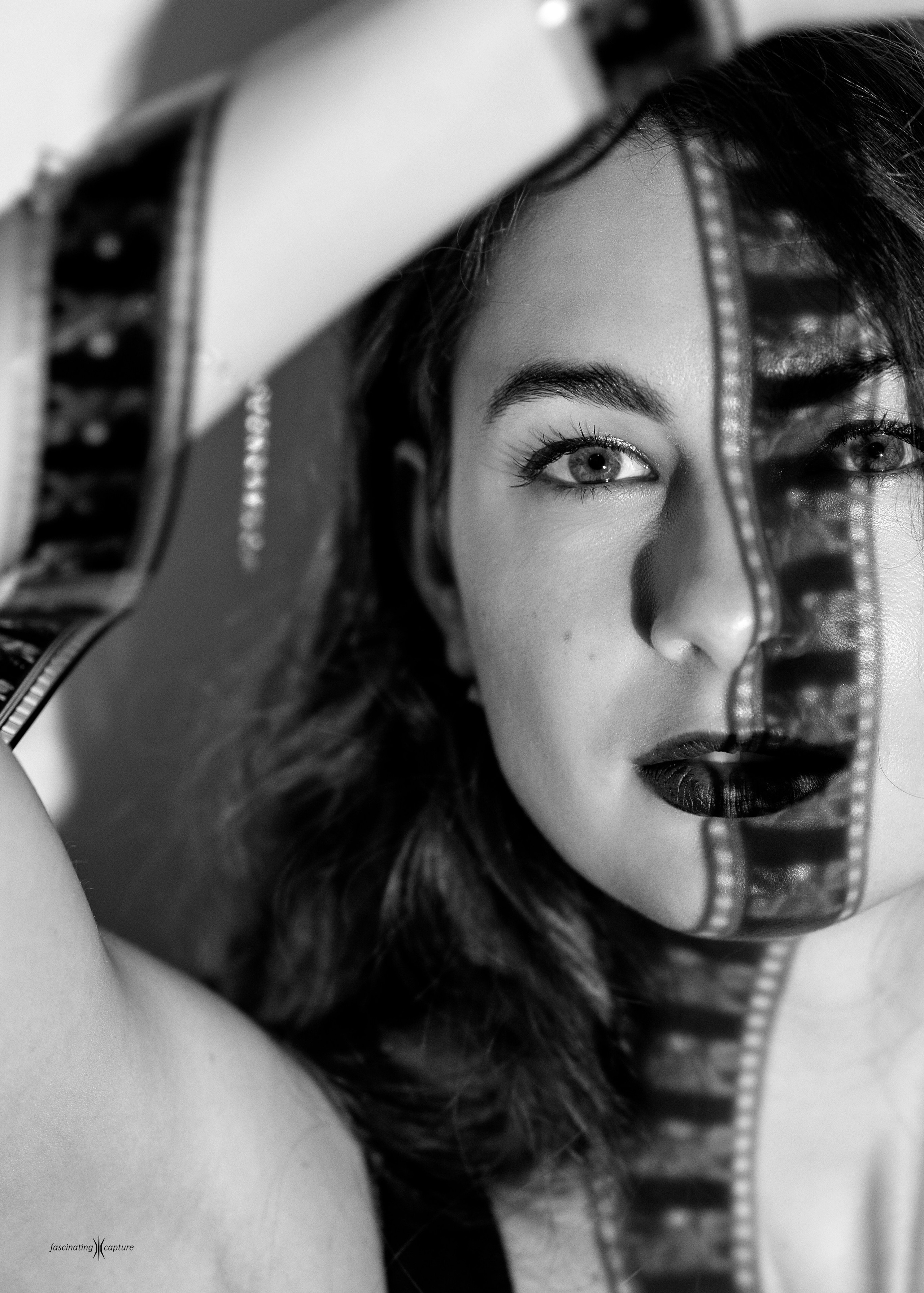 ерно-белый художественный студийный портрет девушки с кинопленкой в руках, оставляющей характерную тень на лице. 