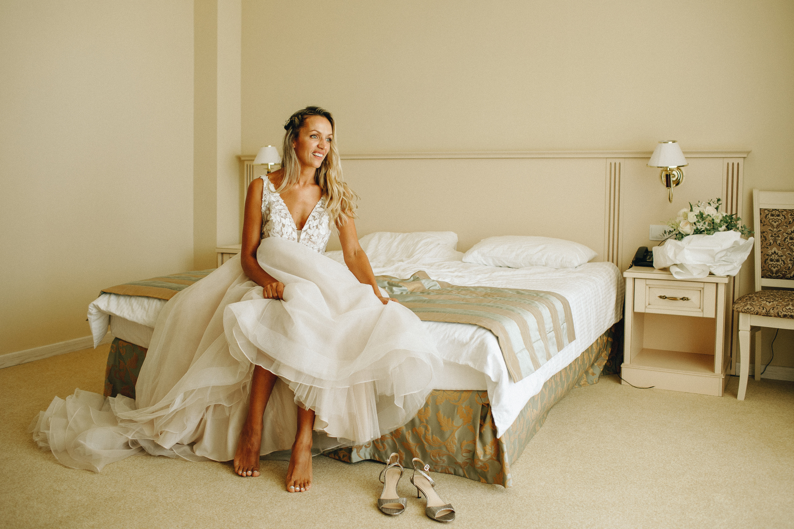 Светлый номер отеля с теплым солнечным светом, невеста присела на кровать для фотографии. Крым фото для души.