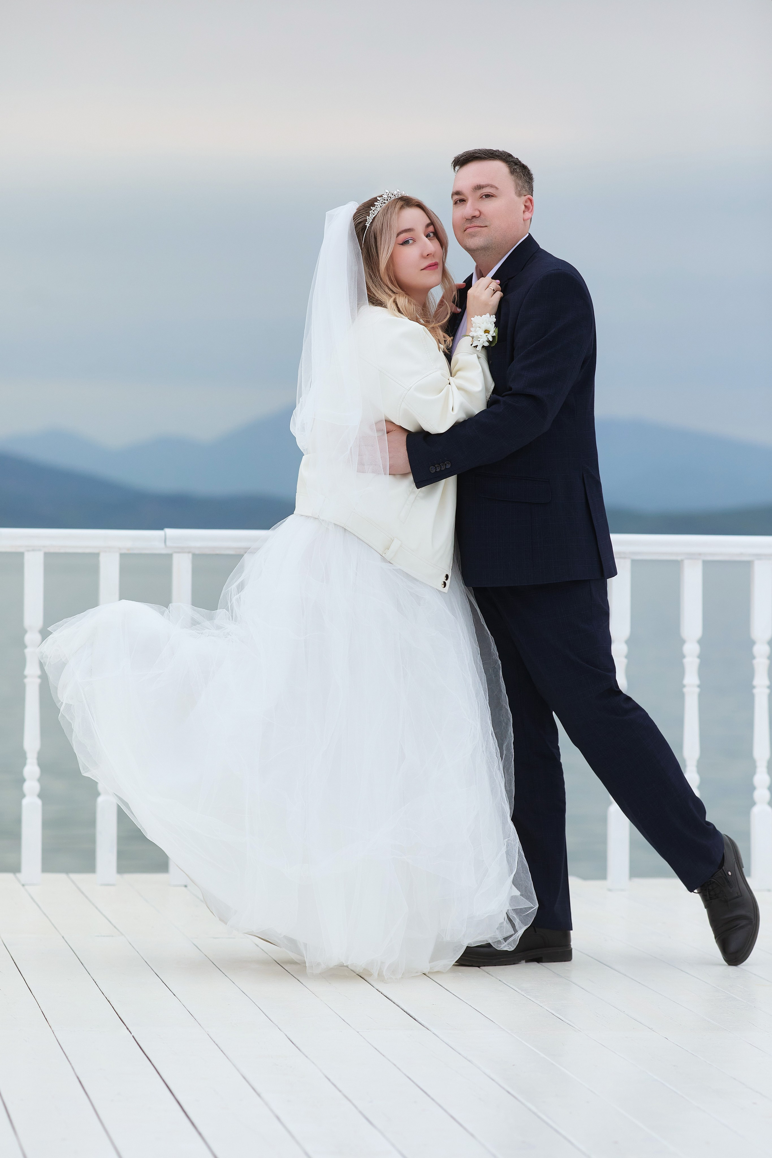 Свадебная фотосессия на фоне штормового моря и белого деревянного парапета