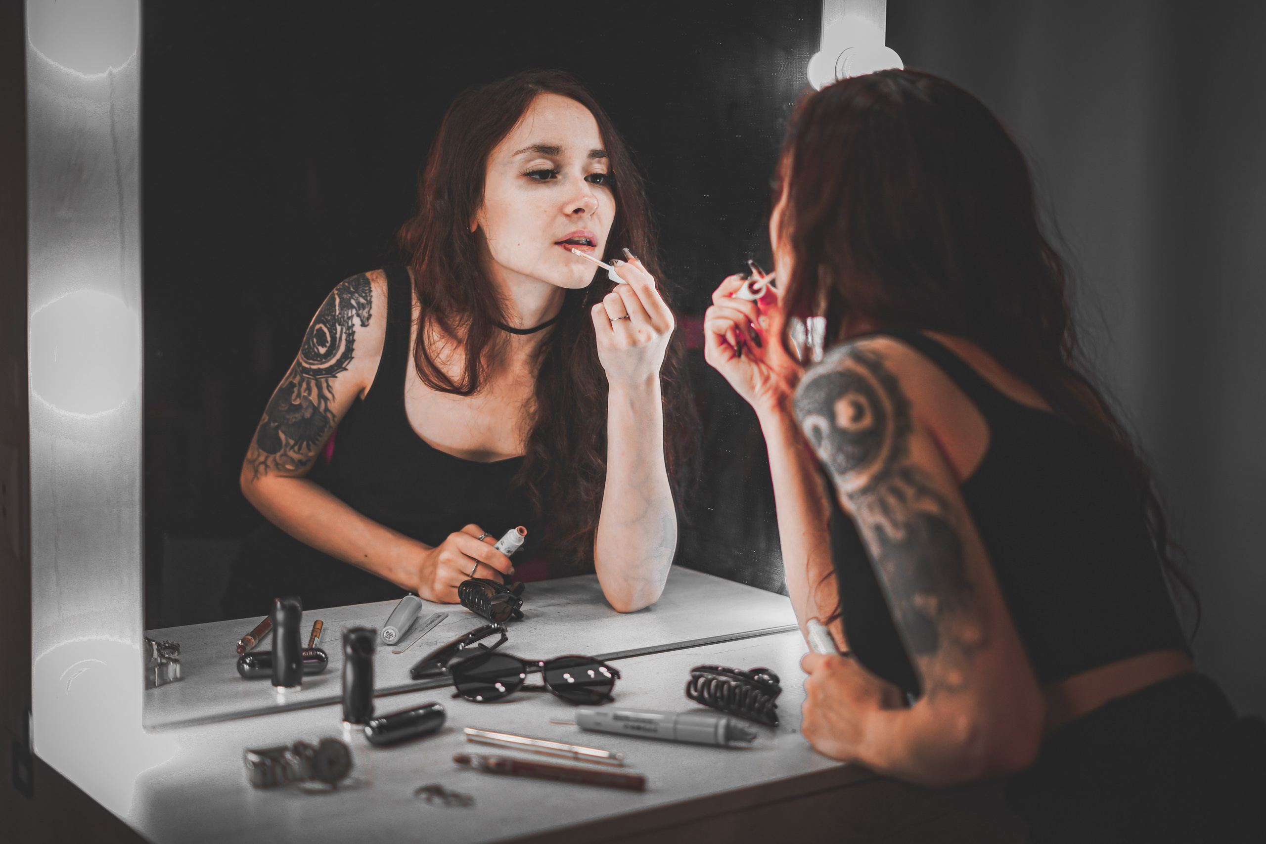 Девушка с тату на руке красит губы у зеркала