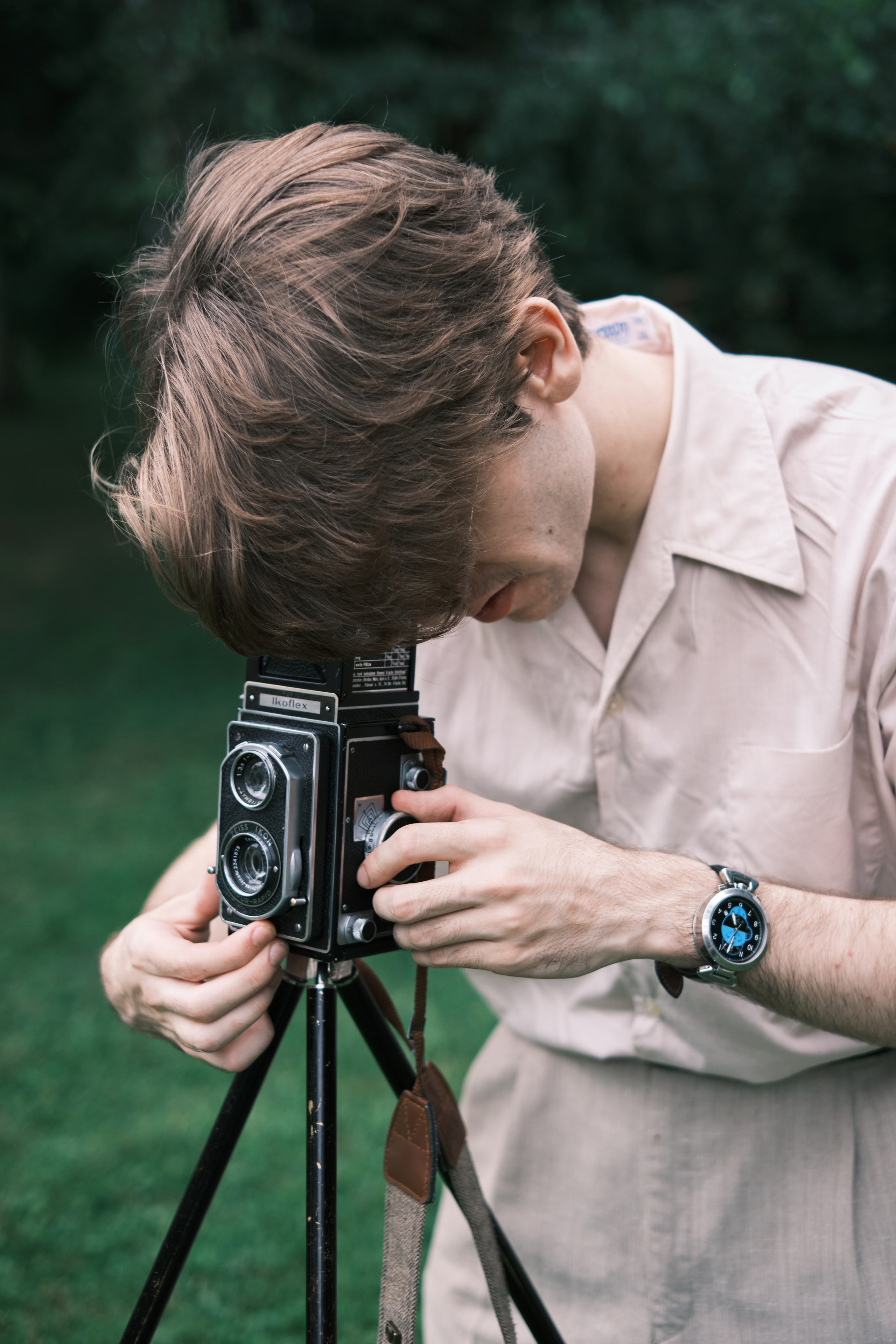 Парень смотрит в старинный пленочный фотоаппарат,  который стоит на треноге