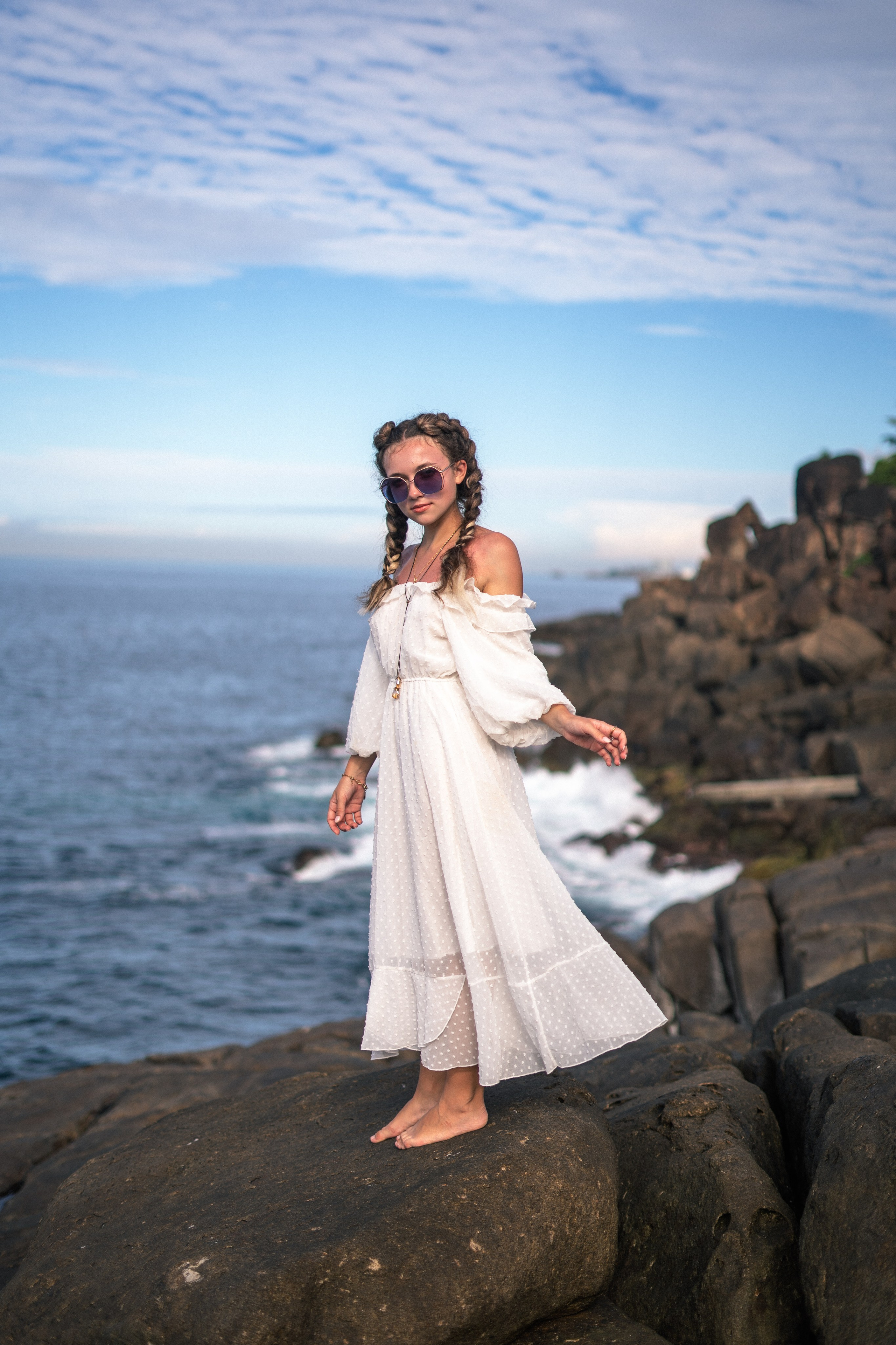 a young girl in a white dress and glasses sitting on the rocks, exposing her legs
