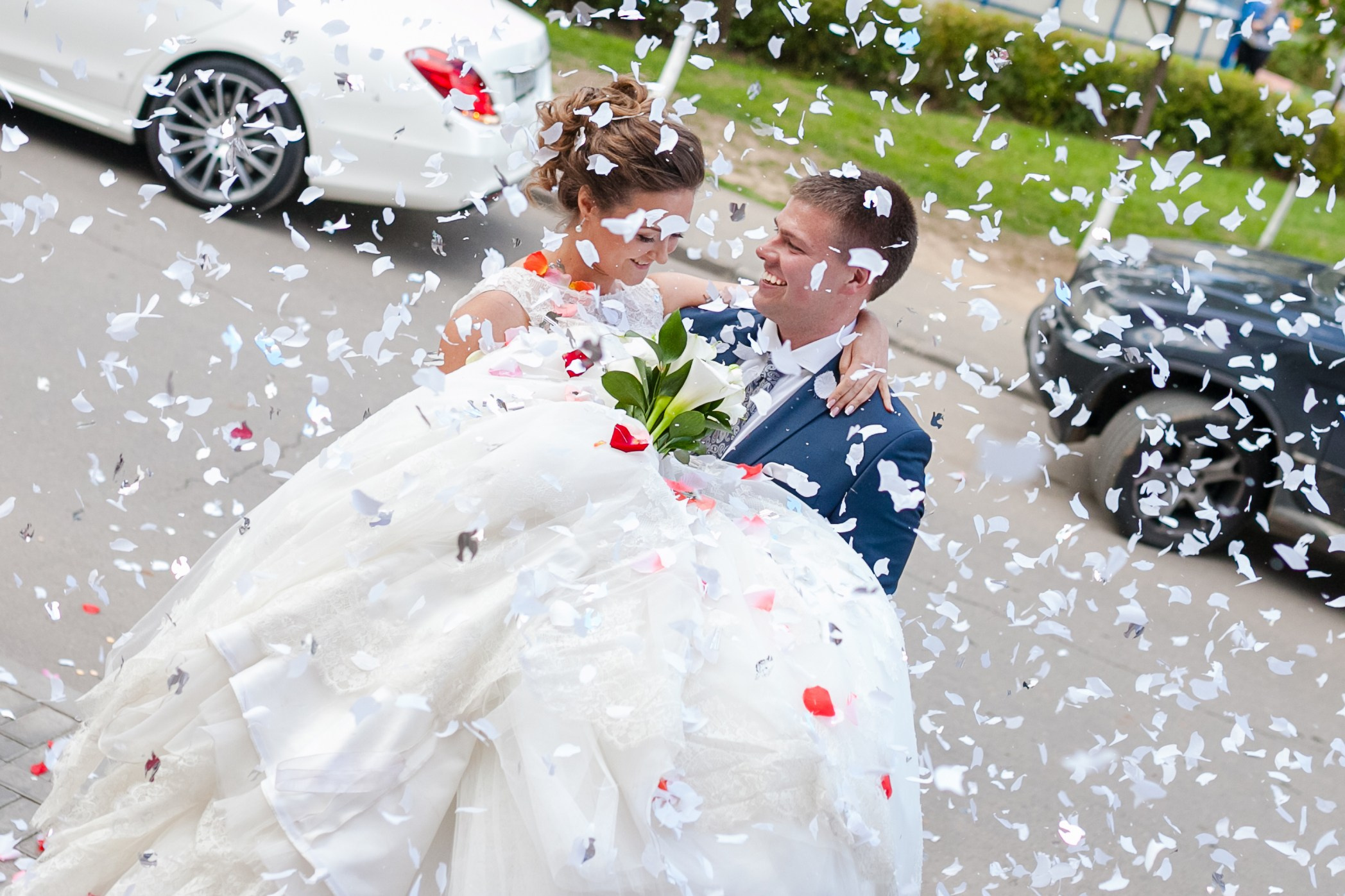 Жених держит на руках невесту под градом лепестков