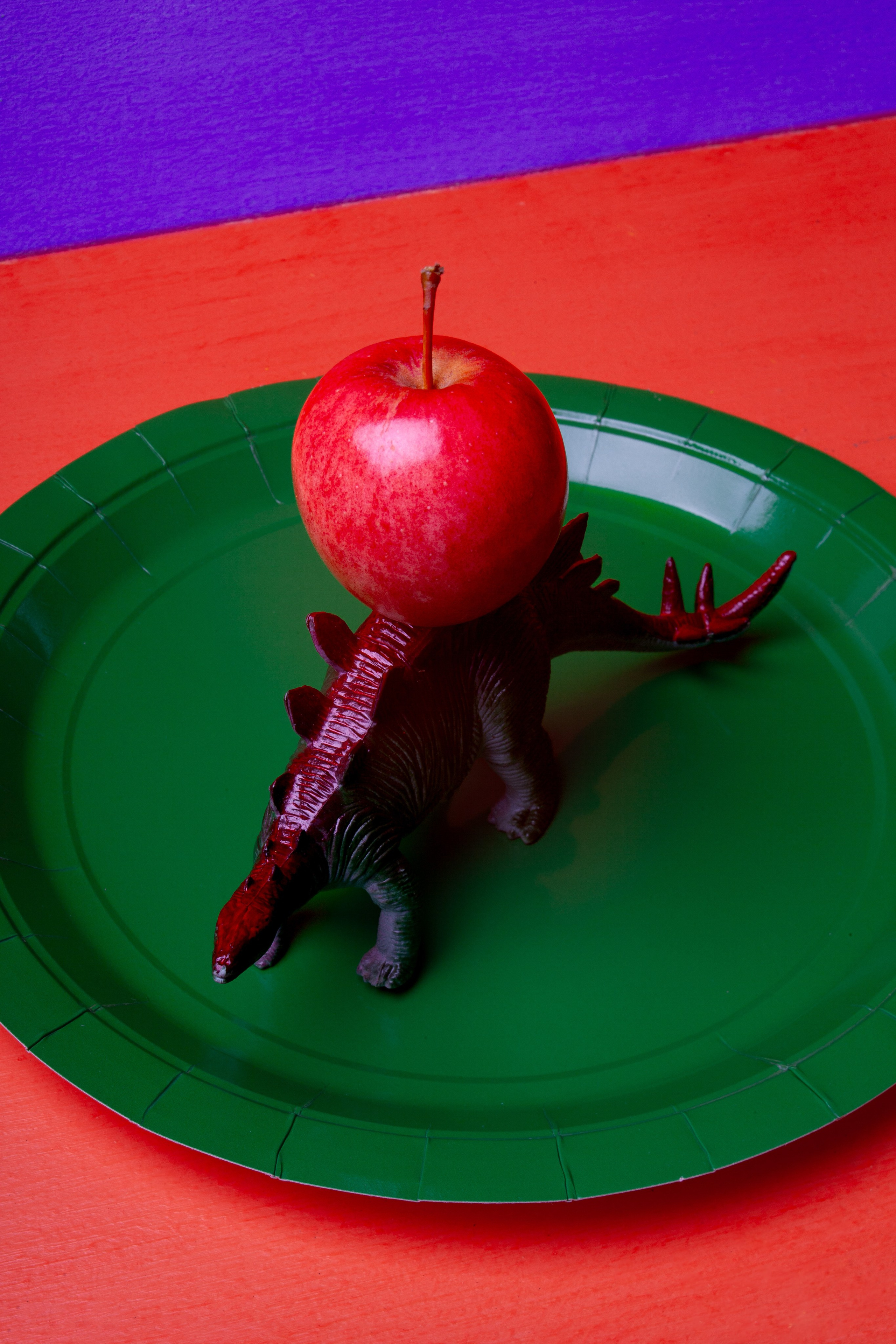 Стегозавр словно ежик несет на спине яблоко на фоне зеленой тарелки
