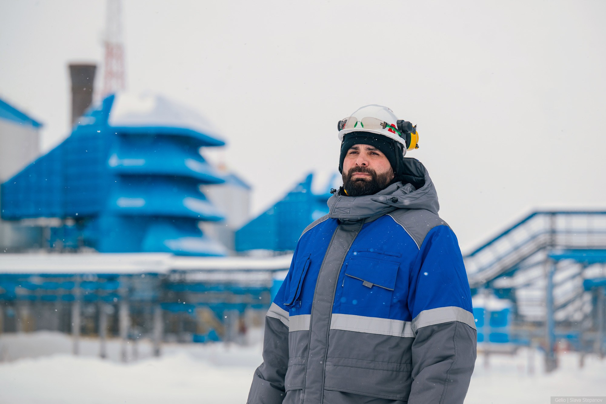 Портрет работника газового промысла с бородой в зимней спецодежде и каске