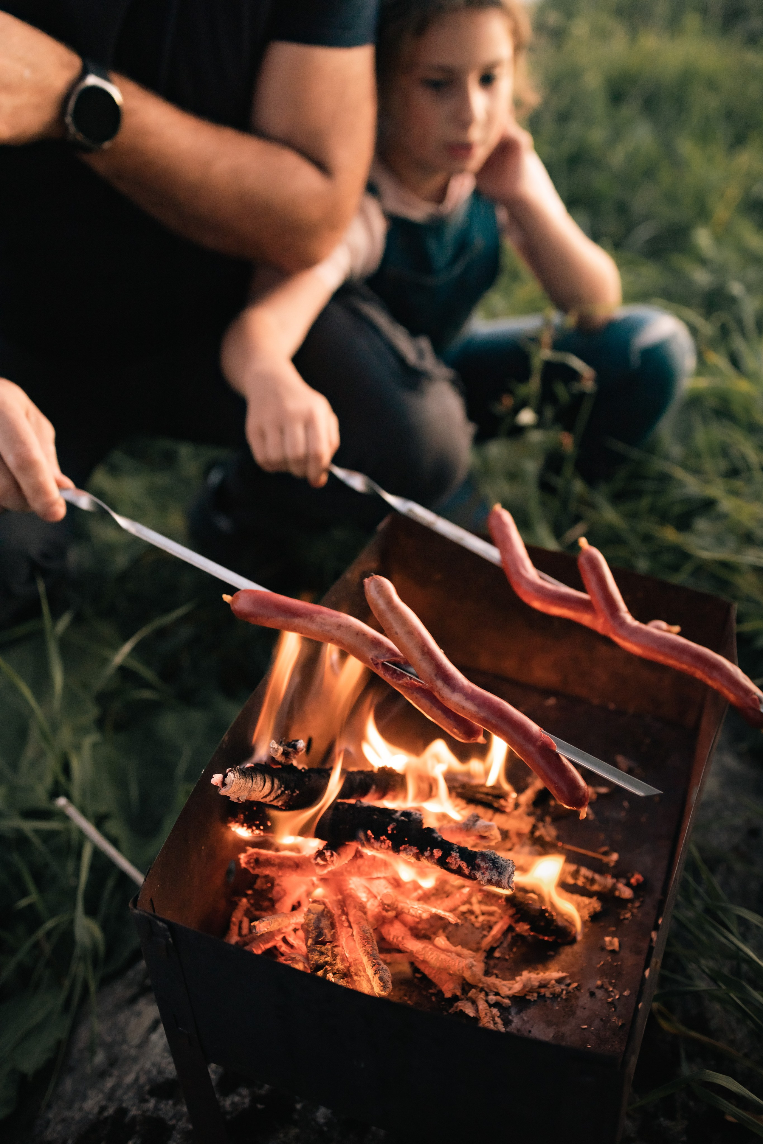 Папа с дочкой готовят ужин на костре, ожидая аппетитных сосисок