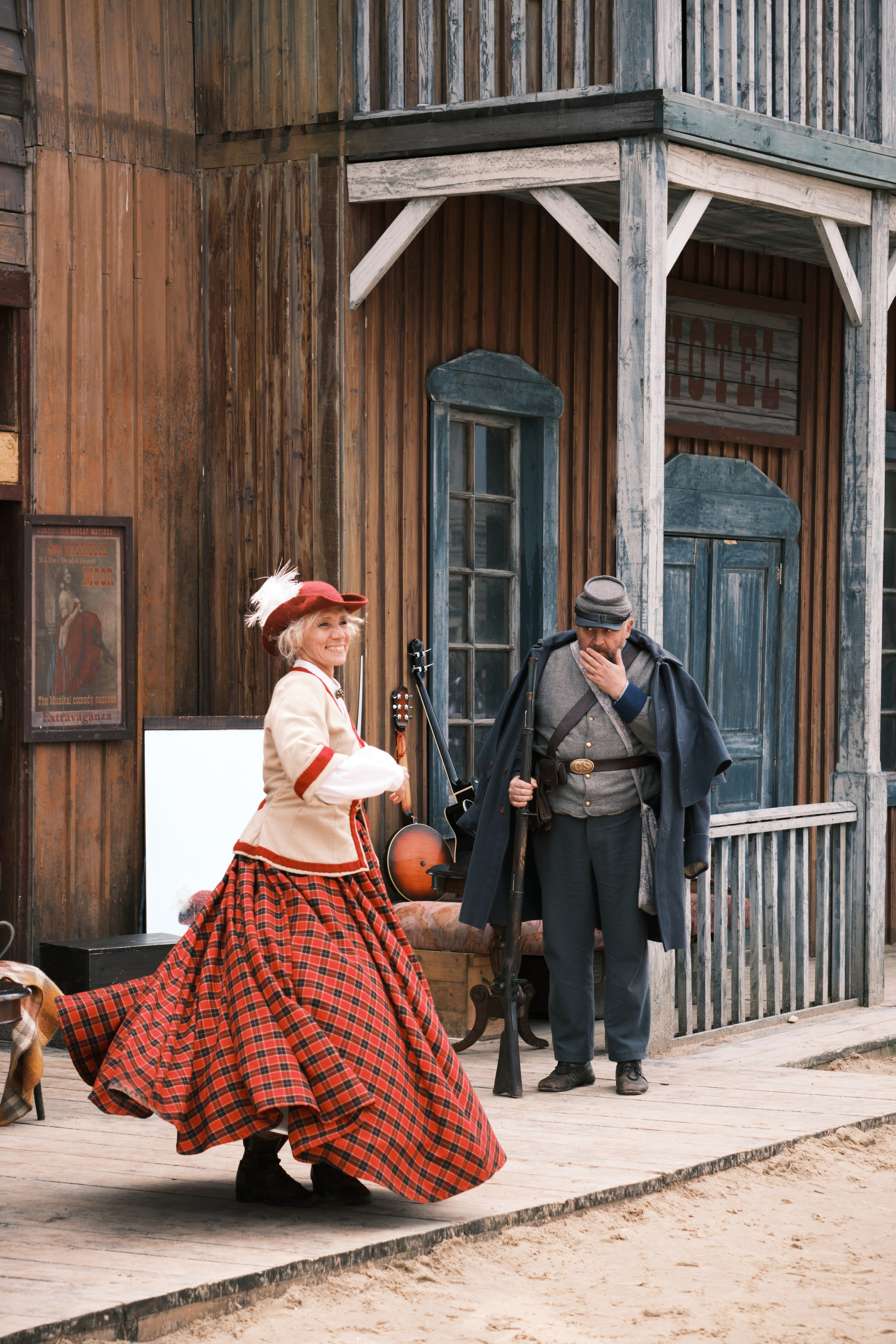 Девушка в красном платье танцует возле салона в ковбойском городке