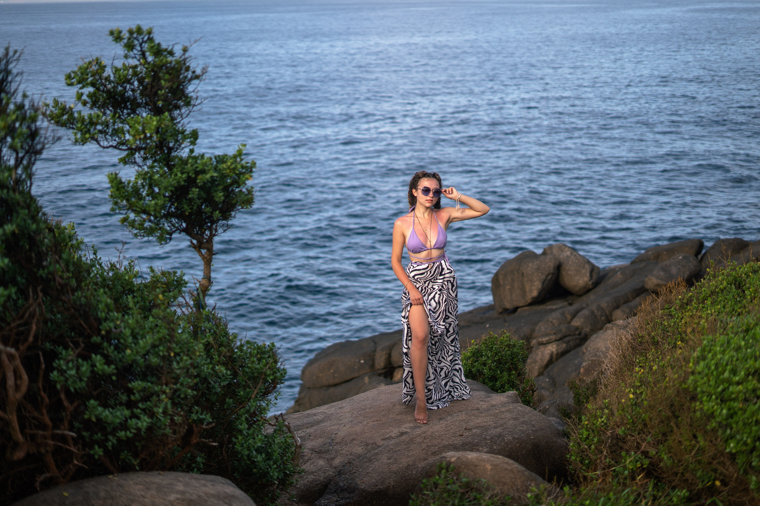 a girl in a purple swimsuit taking stylish shots on the rocks