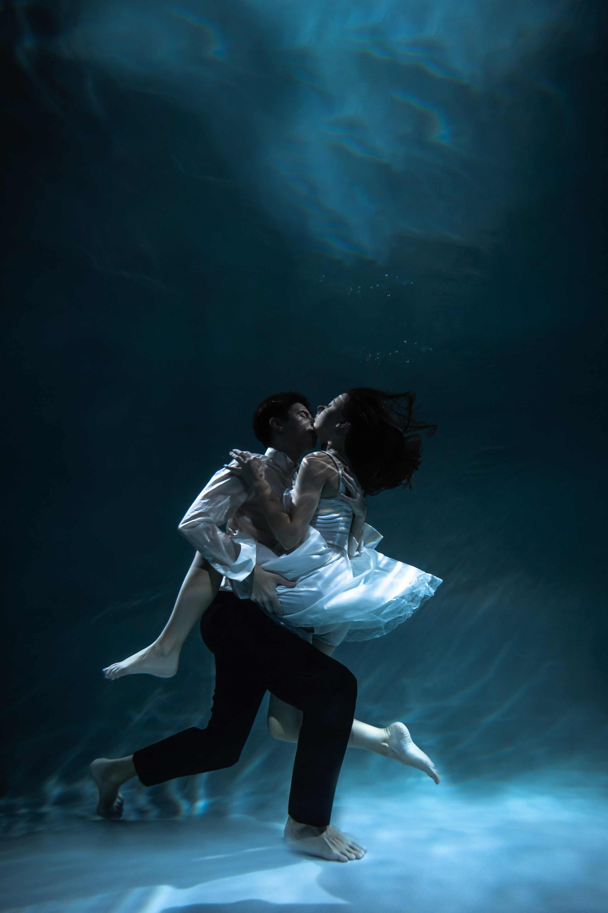 Влюбленная пара погружается в бассейн для творческой фотографии.