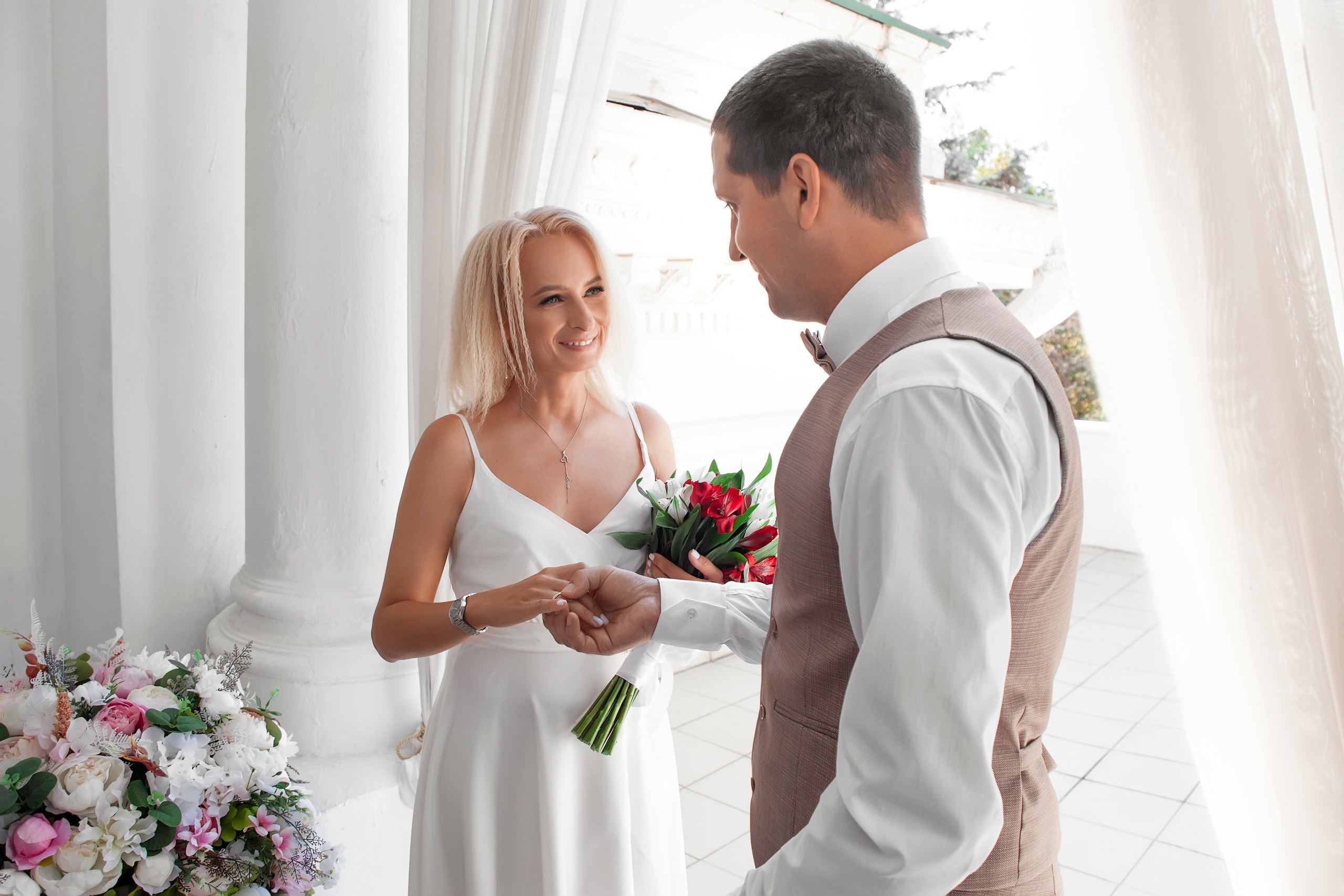 Невеста одевает кольцо на палец жениха и смотрит на его реакцию - свадебное фото в ЗАГСе