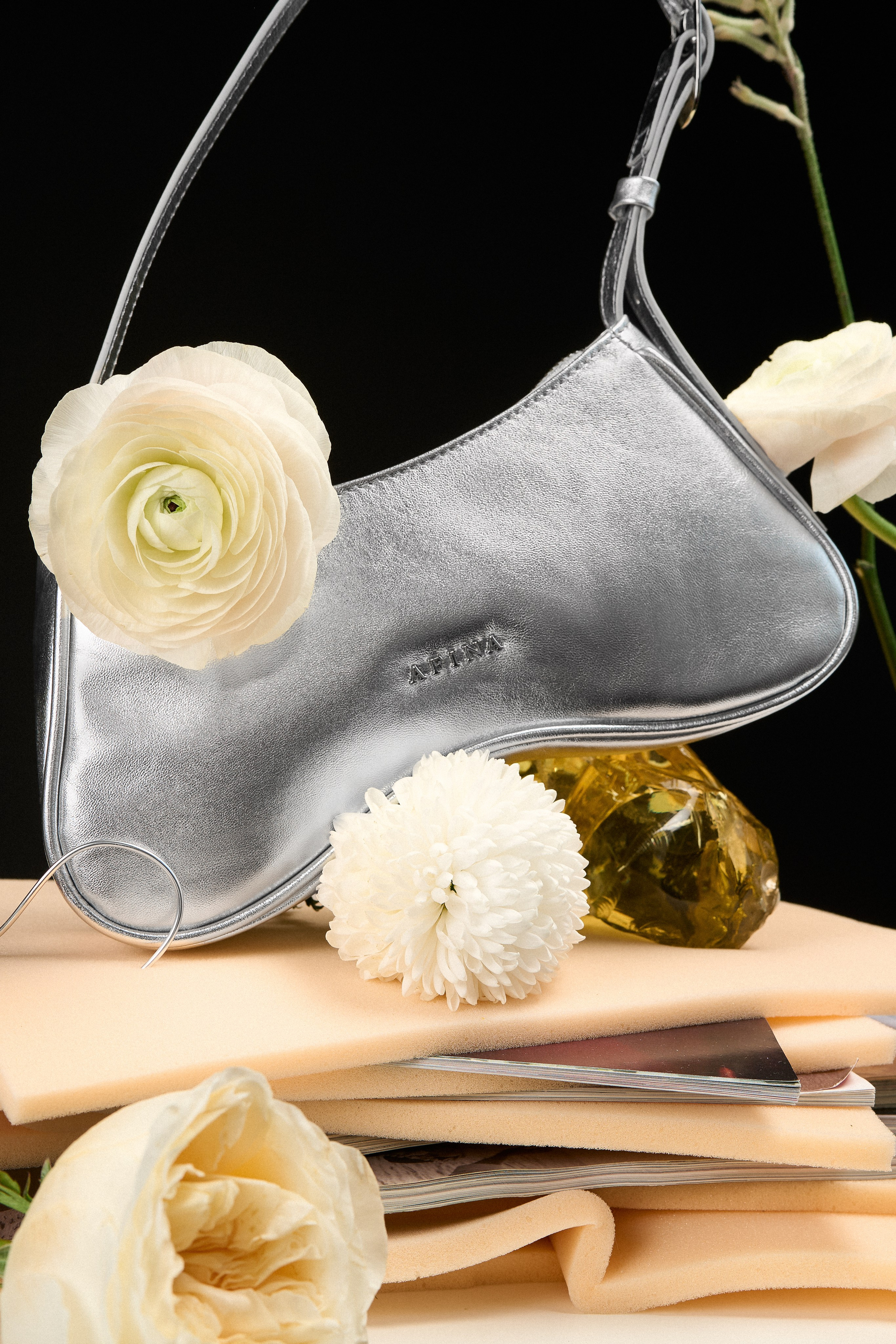Серебряная кожаная сумка Afina Bags среди цветов и декоративных объектов в предметной рекламной съёмке