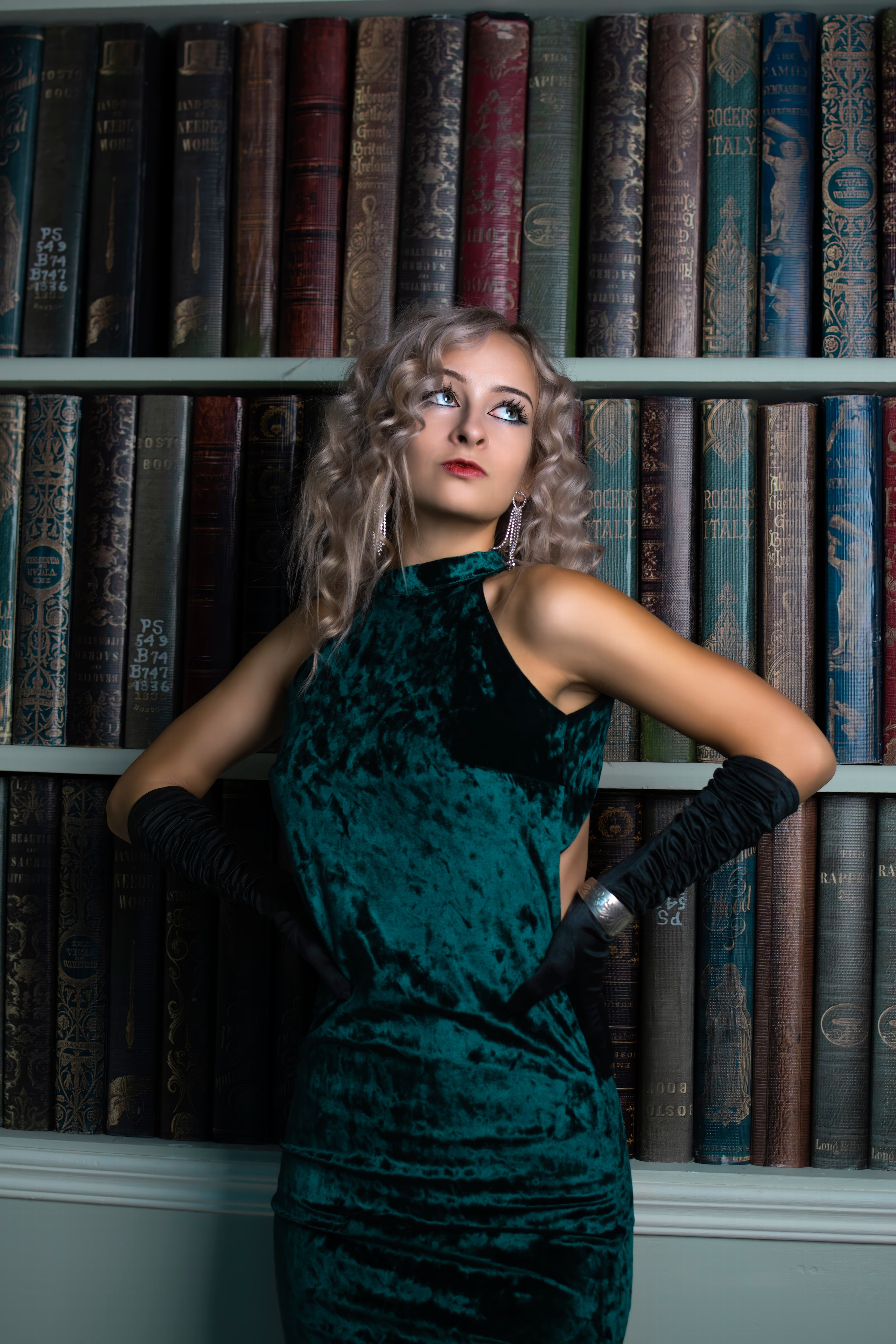 Блондинка в бархатном платье у книжной полки