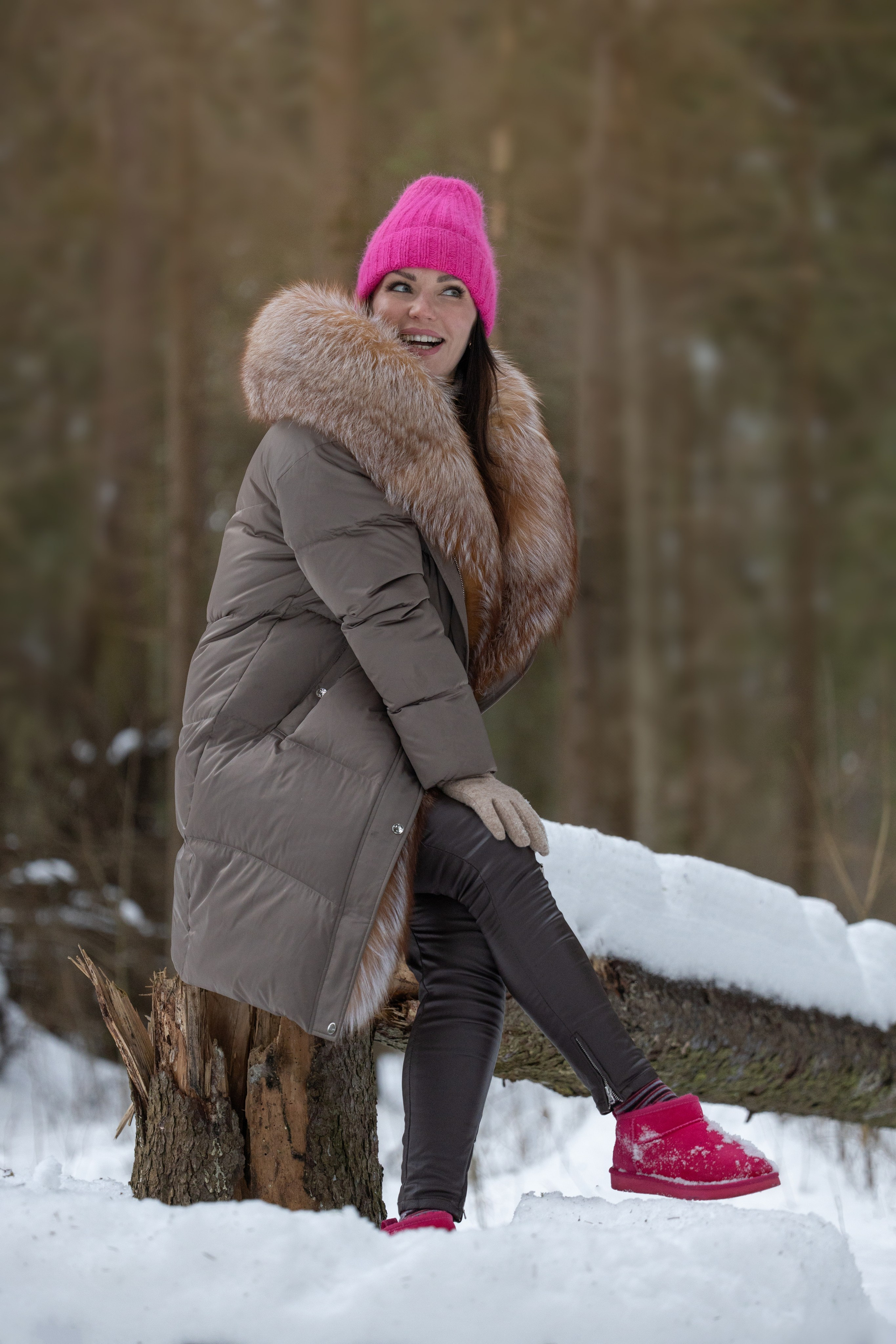 зимняя фотосессия девушка сидит в лесу на пне в розовой шапке и сапогах