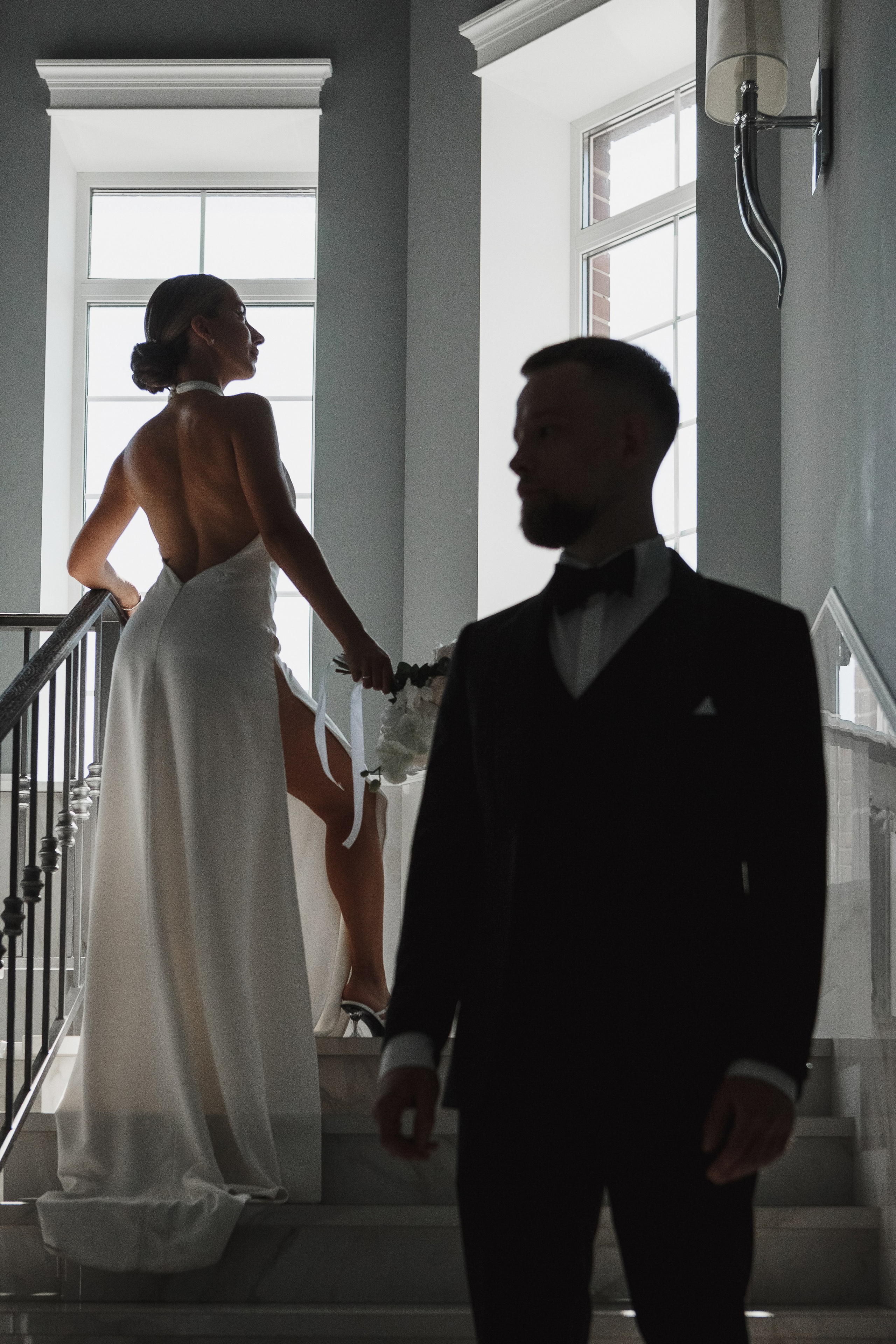 Невеста с букетом поднимается по лестнице комплекса Golden Horse, жених в смокинге в тени, свадебная фотосессия Таганрог