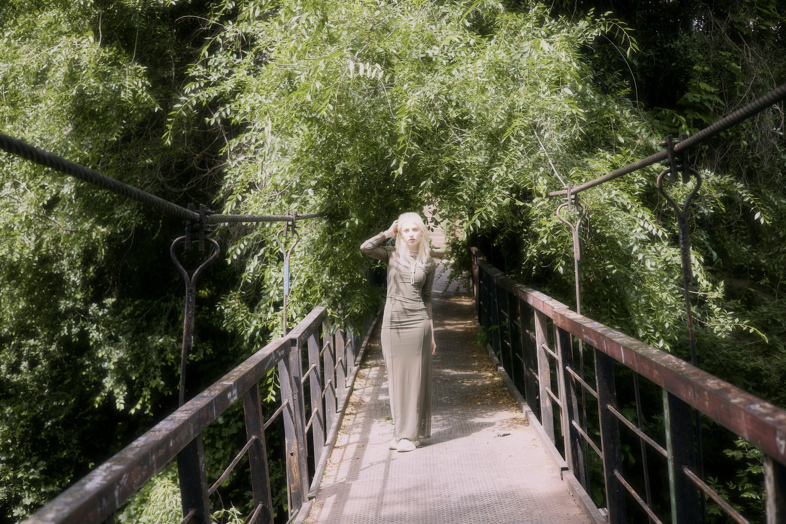 Фотосессия девушки в зелёном платье на мосту в тени деревьев