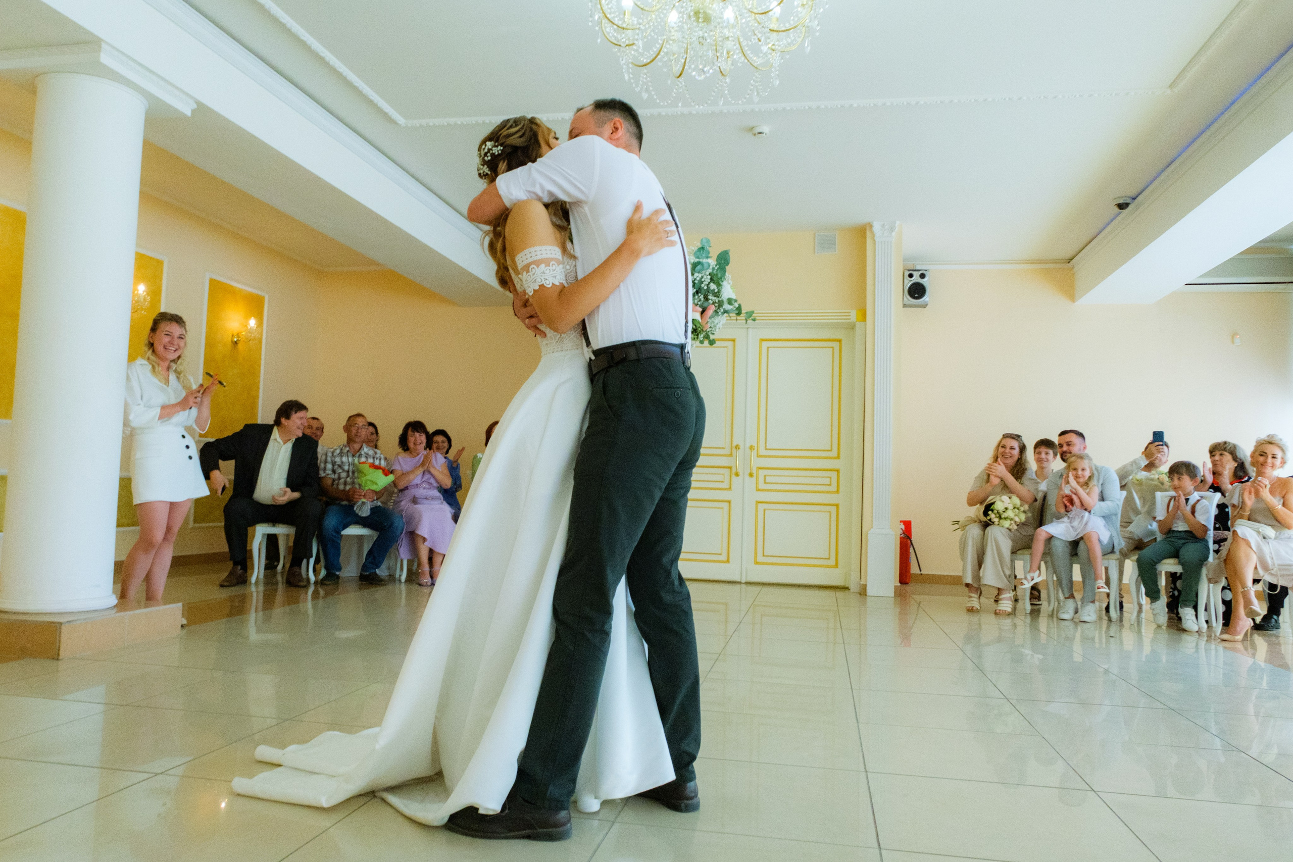  Первый поцелуй после регистрации: молодожены целуются на фоне праздничного декора зала, их лица полны радости.