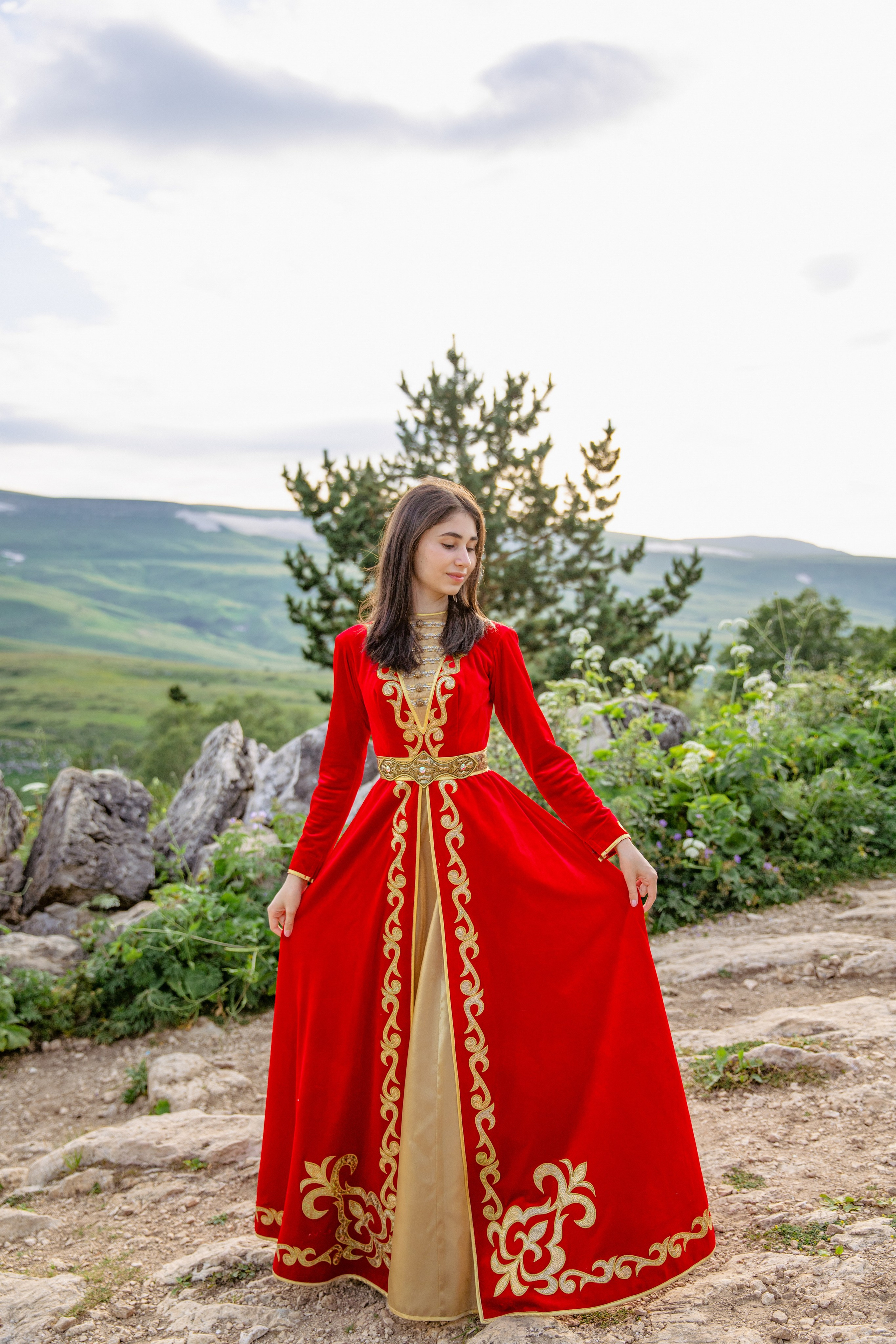 Девушка в адыгейском красном платье с золотым украшением , смотрящая вдаль на фоне гор