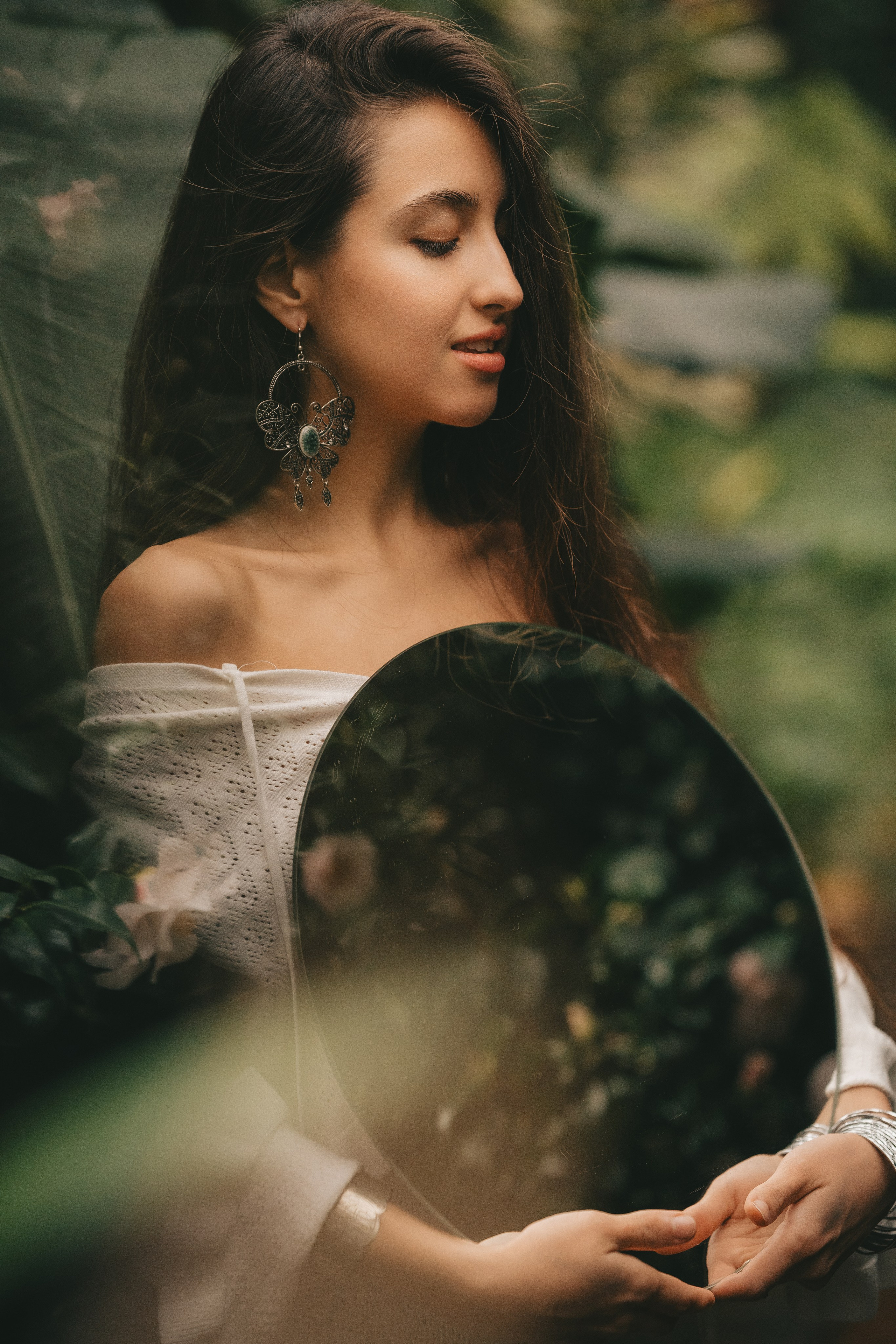 девушка в окружении зеленых растений с зеркалом в руках