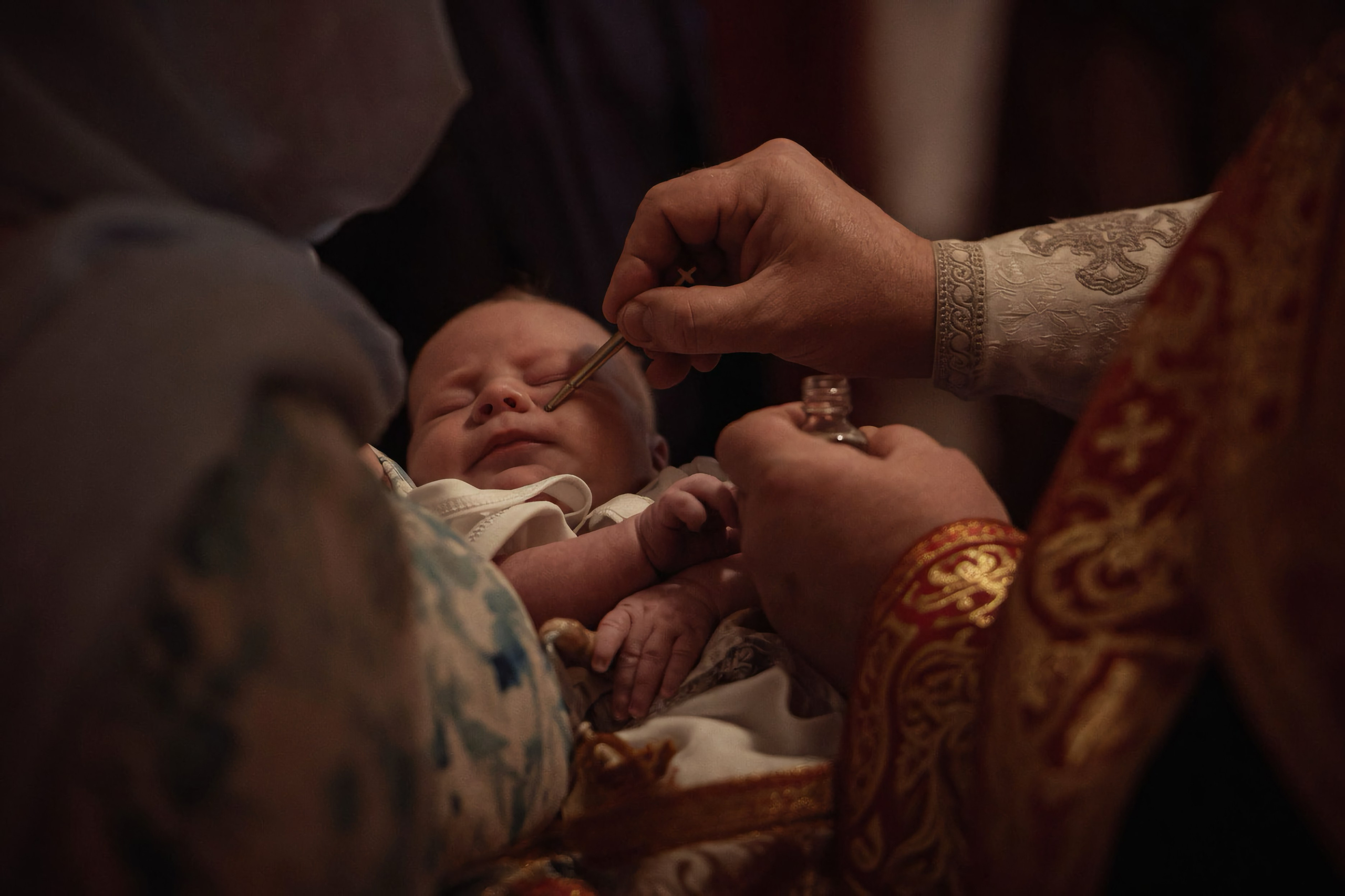 Миропомазание новорождённого — руки священника в красном облачении с кисточкой, тёмный тёплый свет — Екатеринбург, Илья Антропов