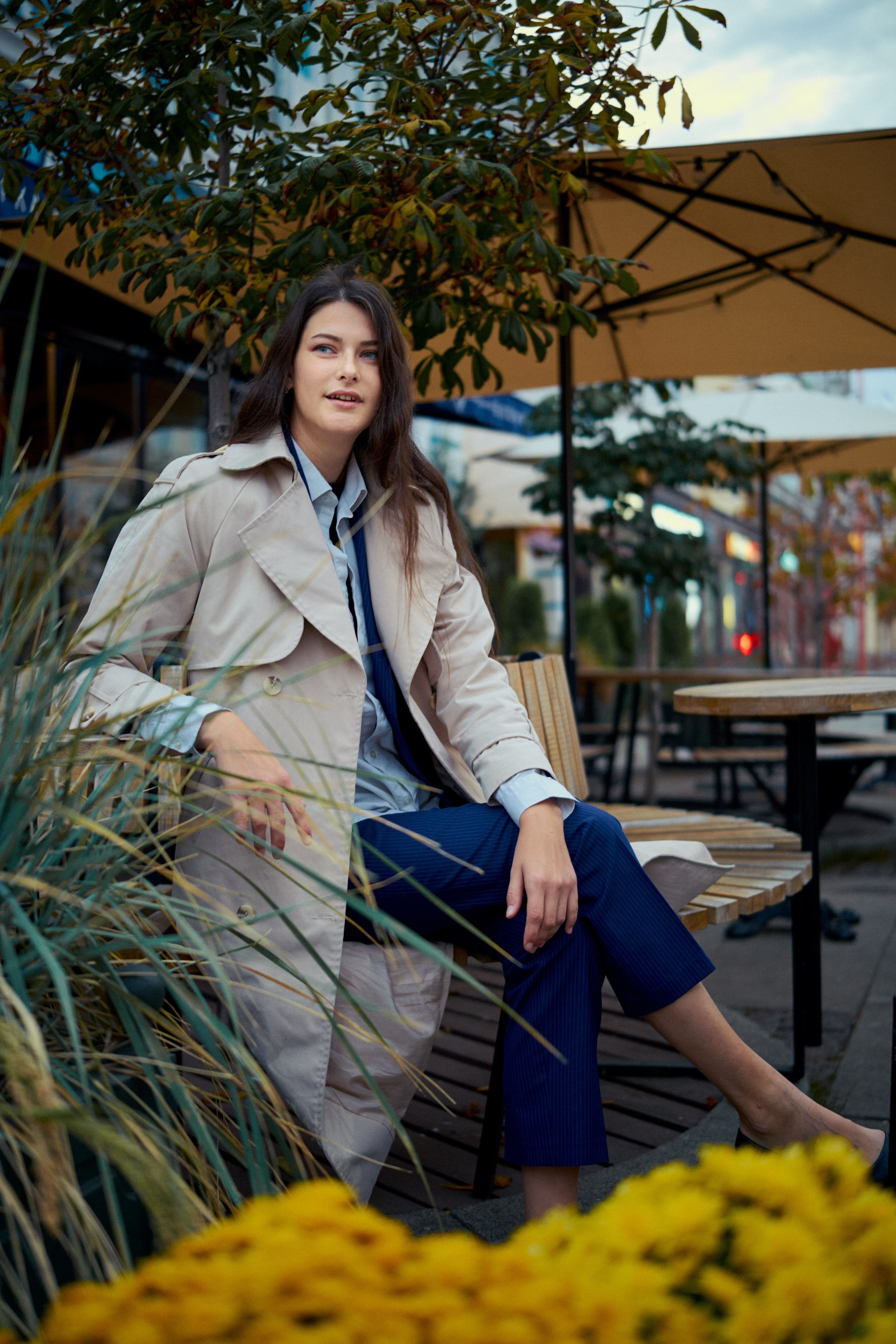 Молодая женщина в бежевом плаще на фоне ярких осенних цветов, создающая теплую и уютную атмосферу