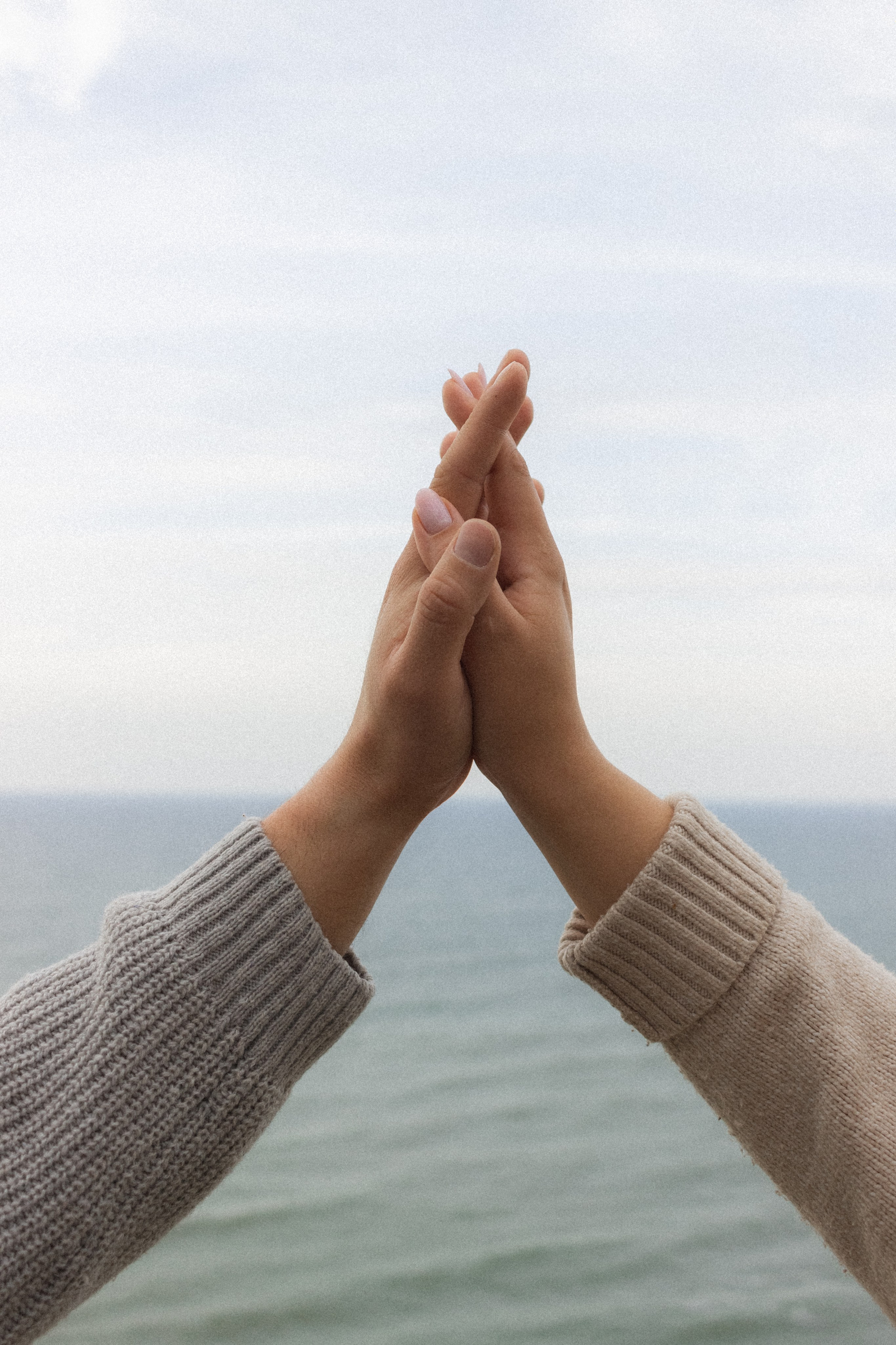 На переднем плане — крупно руки влюбленной пары, на заднем — море.   