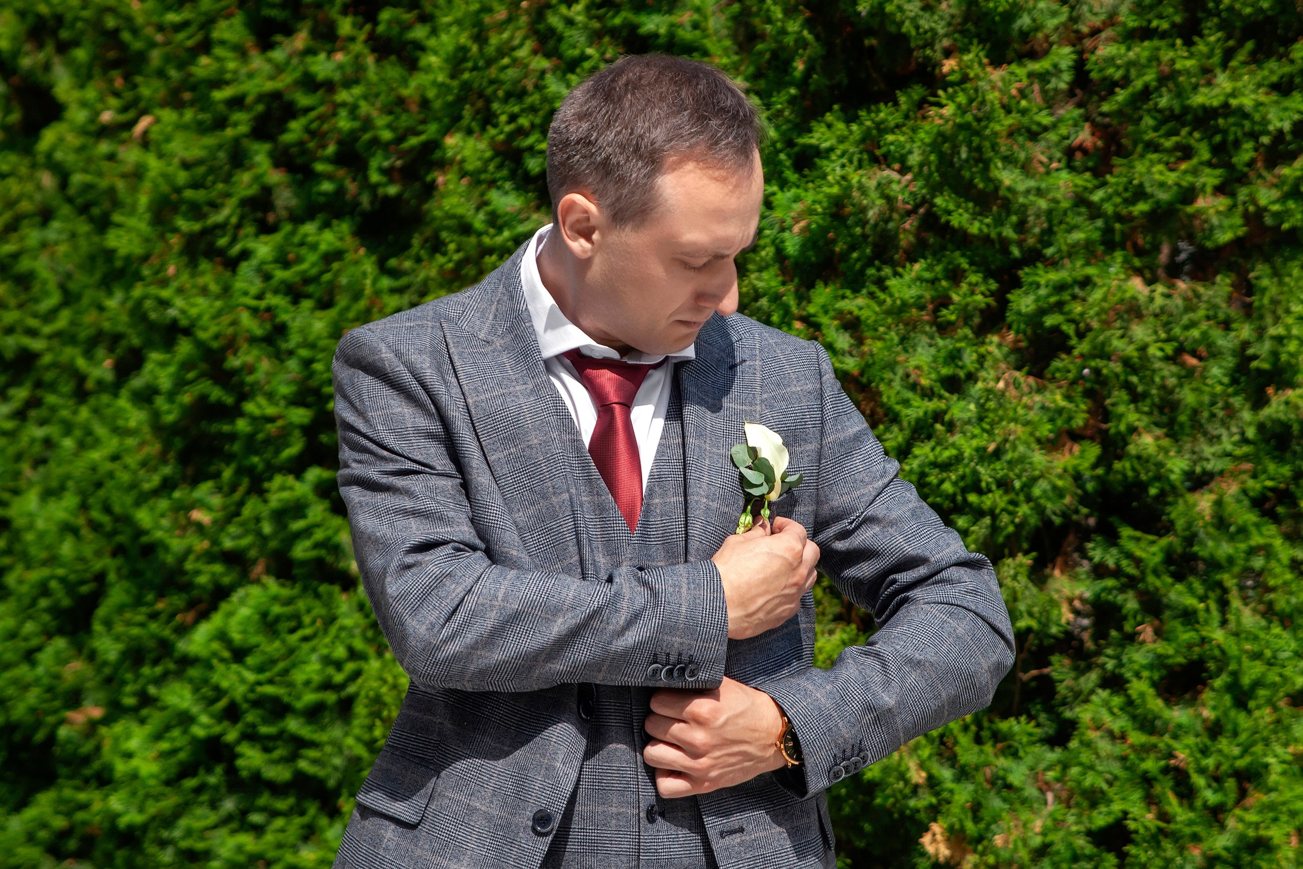 Жених поправляет бутоньерку на фоне зелёных елок
