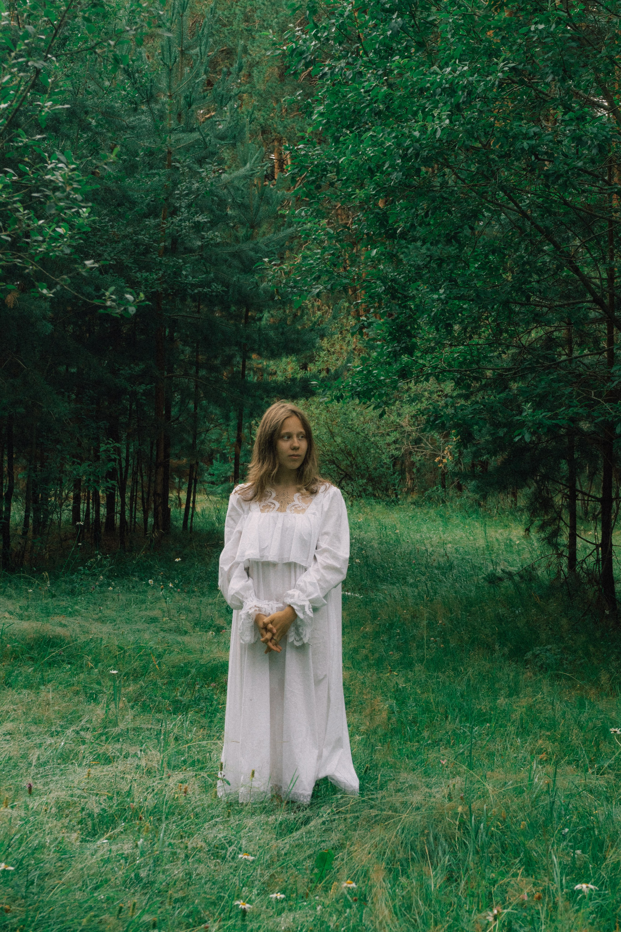 Девушка в белом платье стоит посреди леса