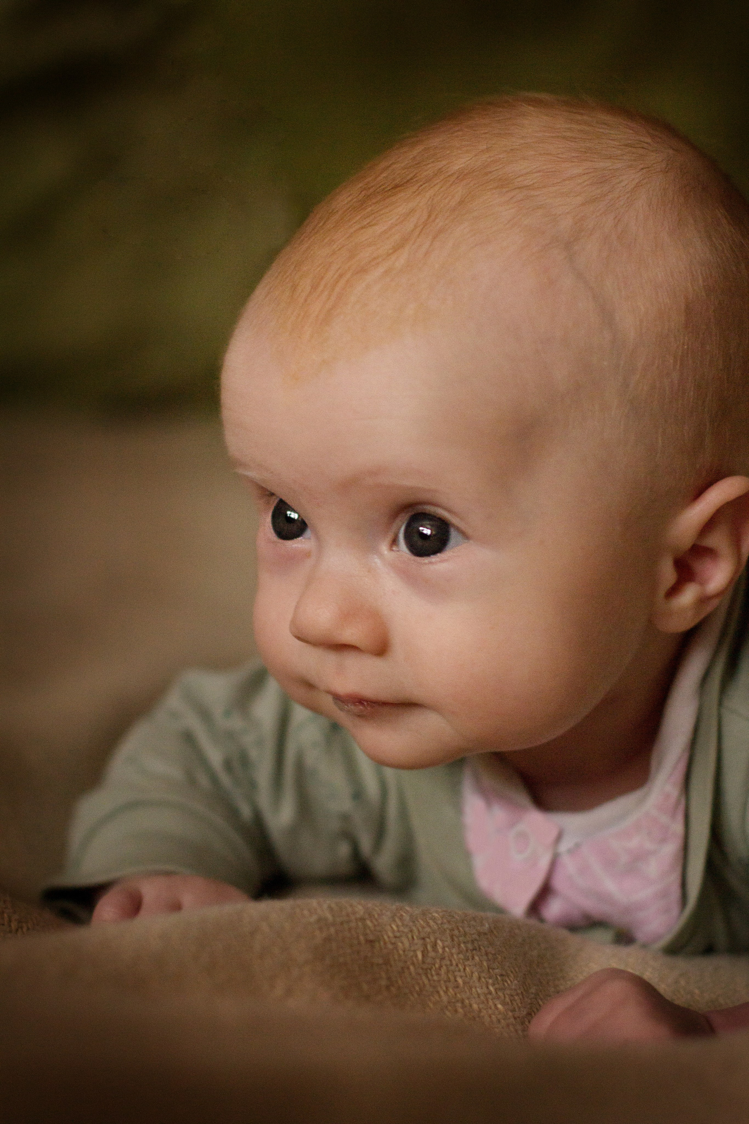 Портрет девочки младенца в розово-зелёной кофточке крупным планом лёжа на диване