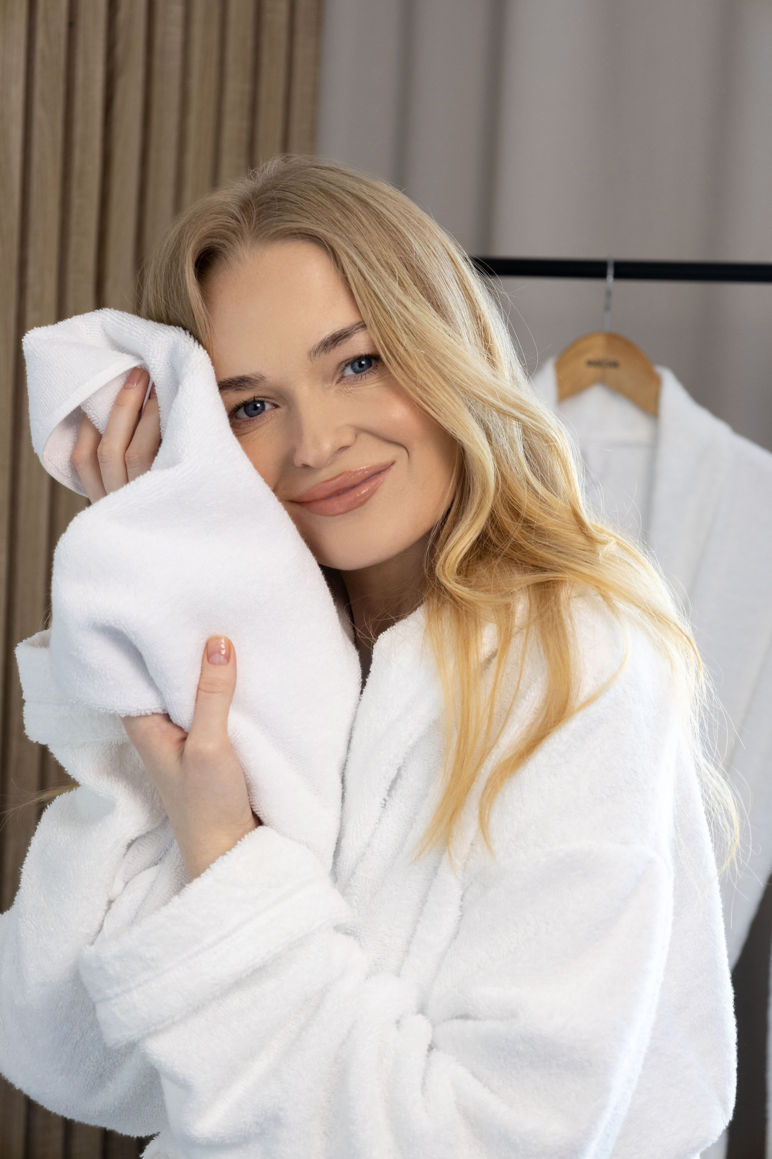 Девушка в белом халате прижимает полотенце к лицу | Интерьерная съемка для бренда