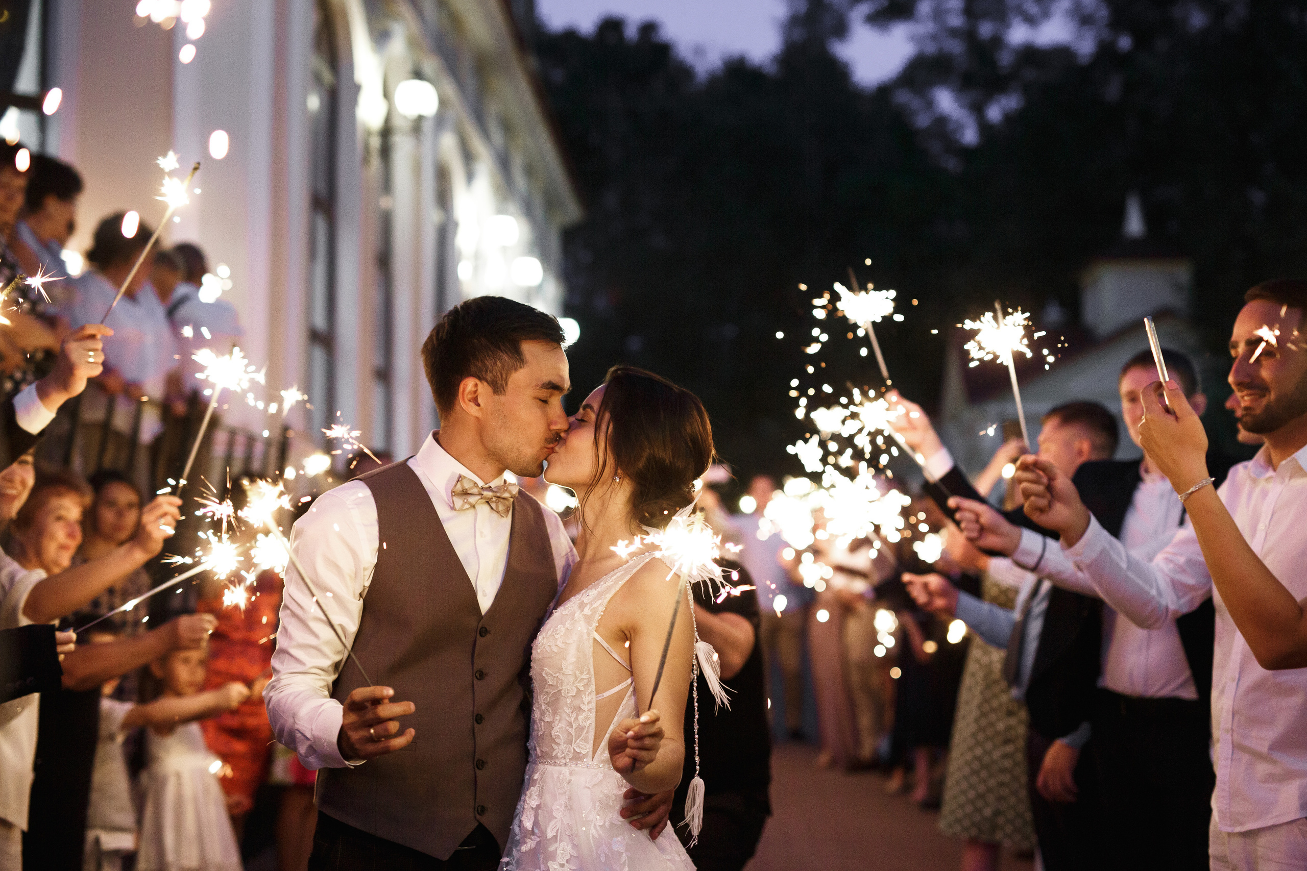 жених и невеста целуются в конце банкета на фоне бенгальских огней